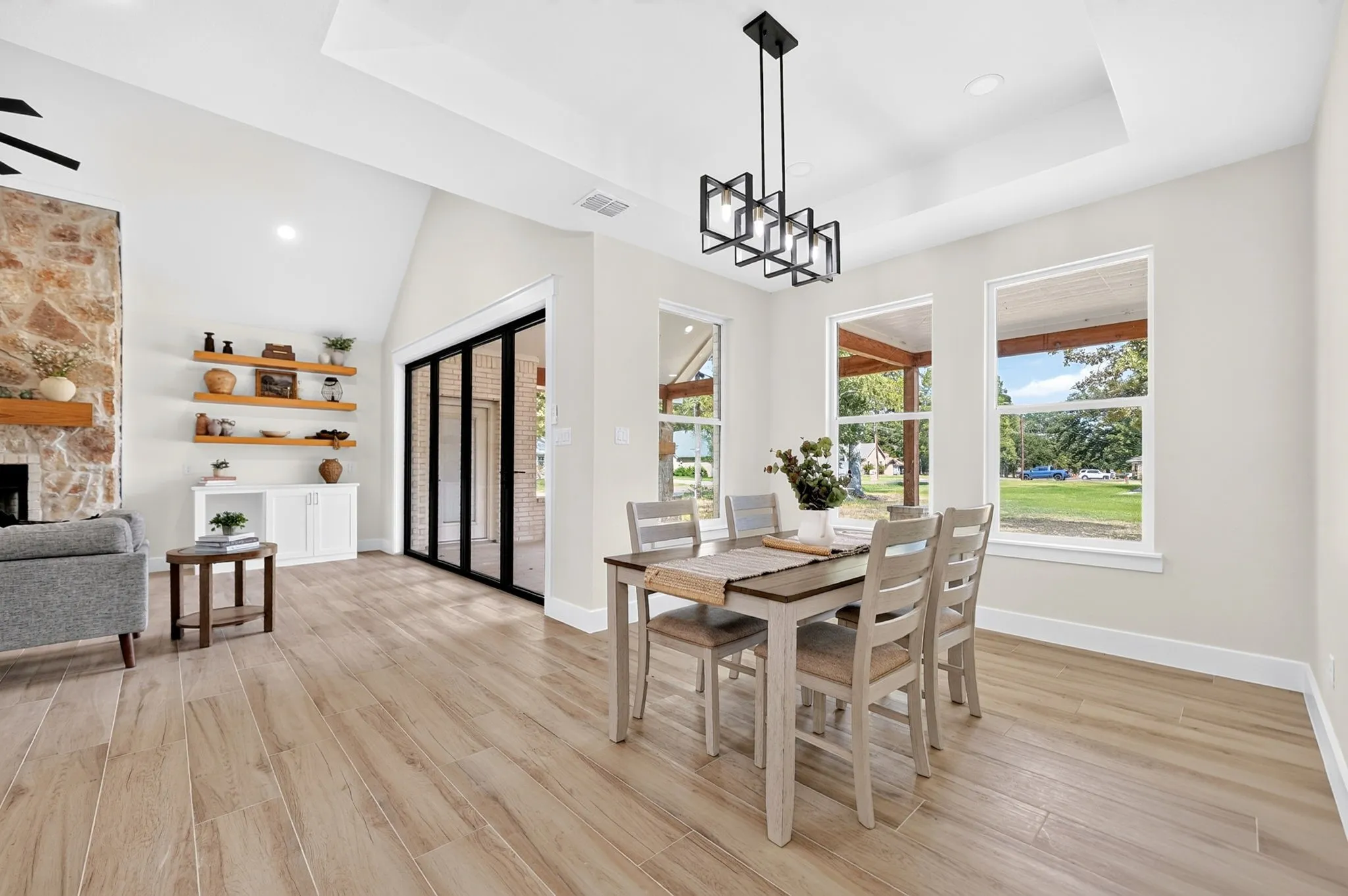 Vaulted ceilings with recessed lighting, stone fireplace with wood mantel, wood-finish flooring, built-in shelving, and folding glass panel doors