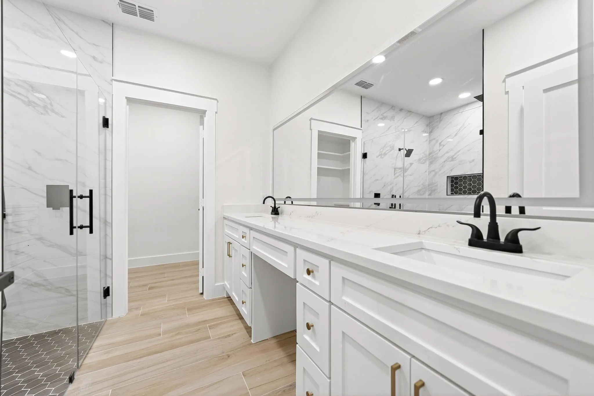 White shaker cabinetry with gold-tone hardware, a dual vanity with undermount sinks, and a full-width mirror