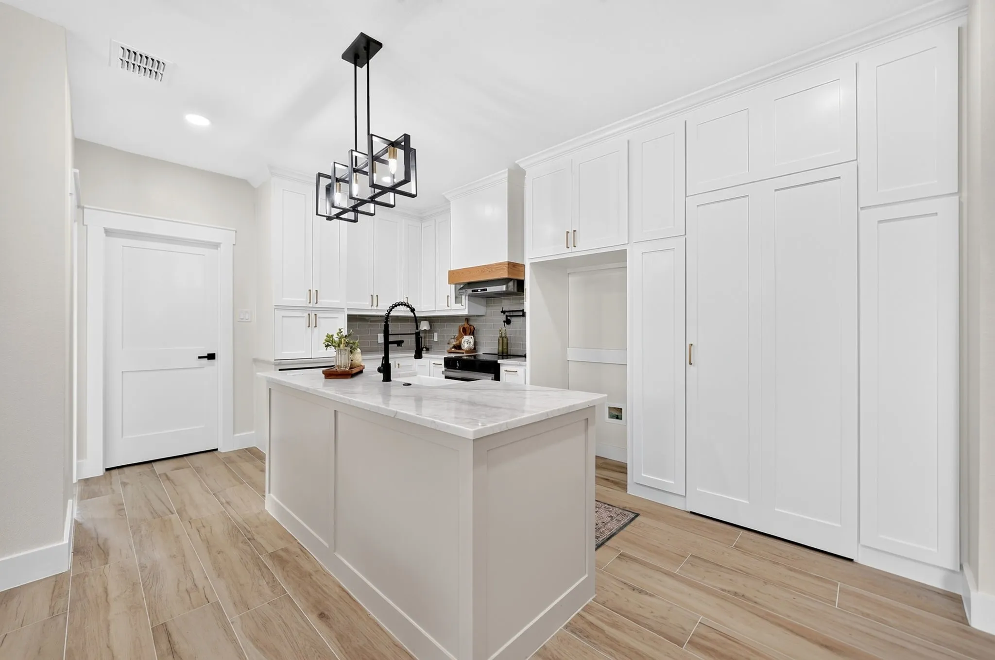 Kitchen featuring an island with stone countertop, white cabinetry with crown molding, wood-finish flooring, and a modern light fixture