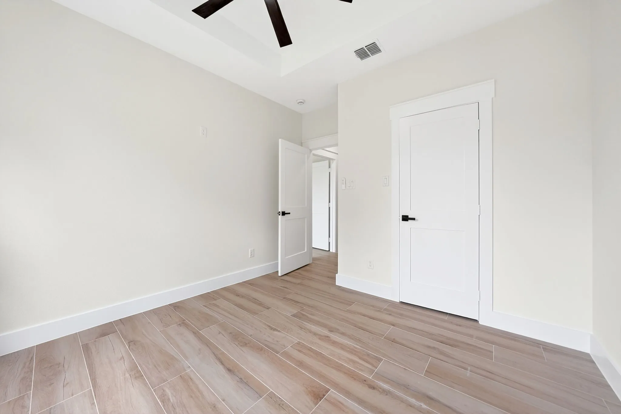 Tray ceiling with a ceiling fan, wood-finish tile flooring, and white interior doors with dark hardware