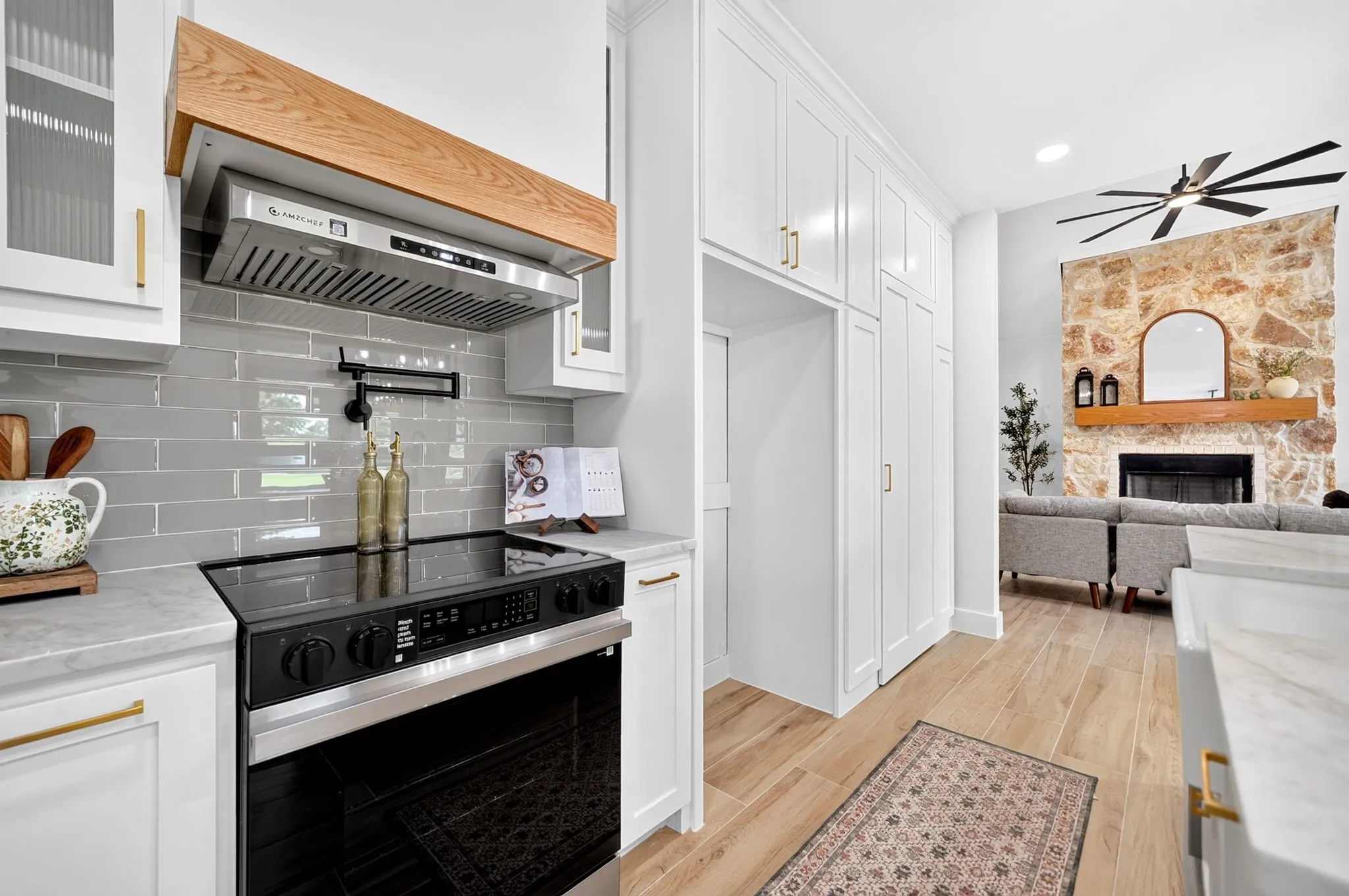 Modern kitchen featuring a built-in oven, sleek range hood with wood trim, and subway tile backsplash