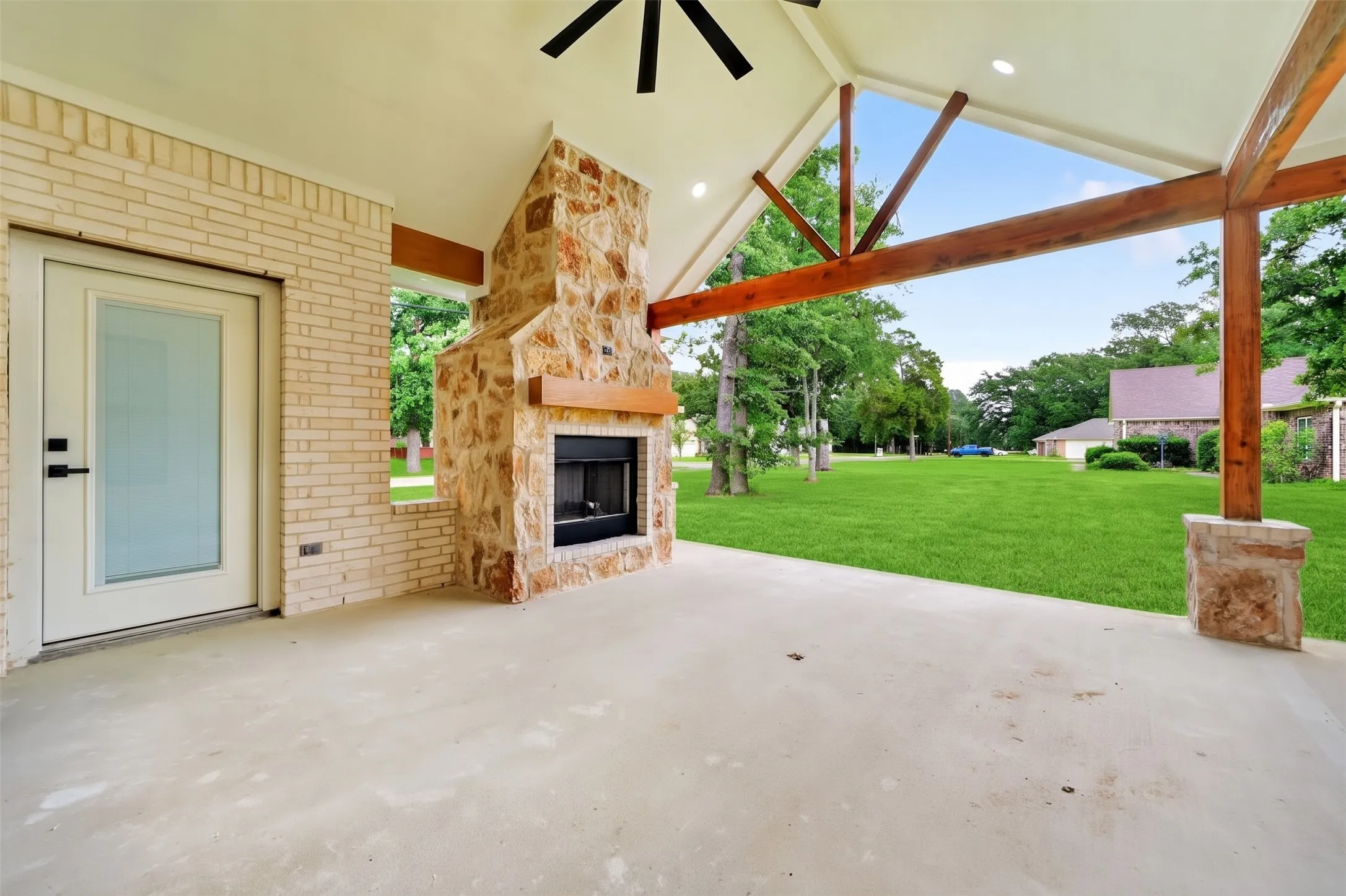 Covered patio featuring an outdoor fireplace with stone surround, wood mantel, and concrete flooring