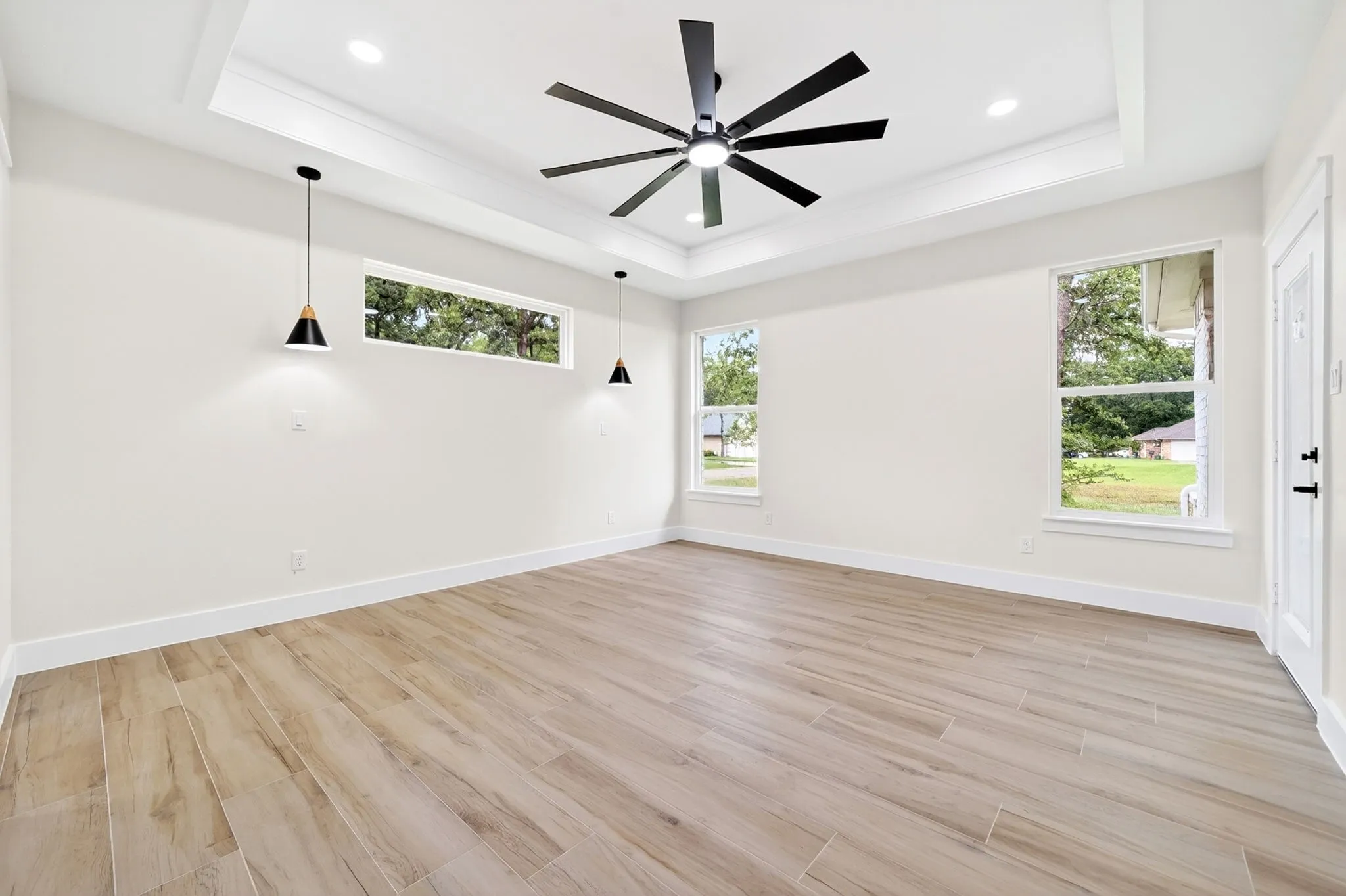 Tray ceiling with recessed lighting, wood-finish flooring, and multiple windows