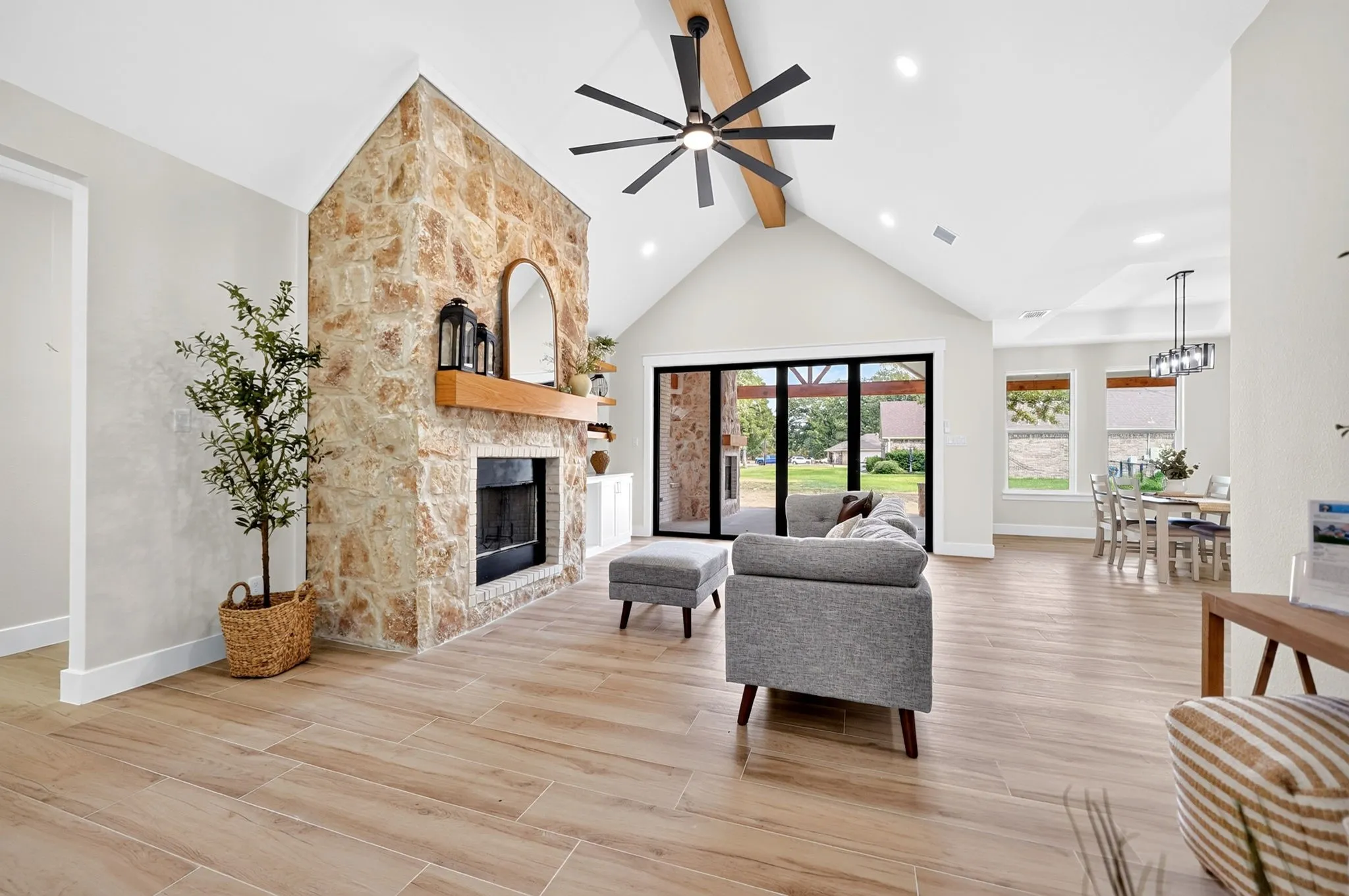Stone-clad fireplace with wood mantel, vaulted ceiling with exposed beam, wood-finish flooring, recessed lighting, and multi-panel sliding glass doors