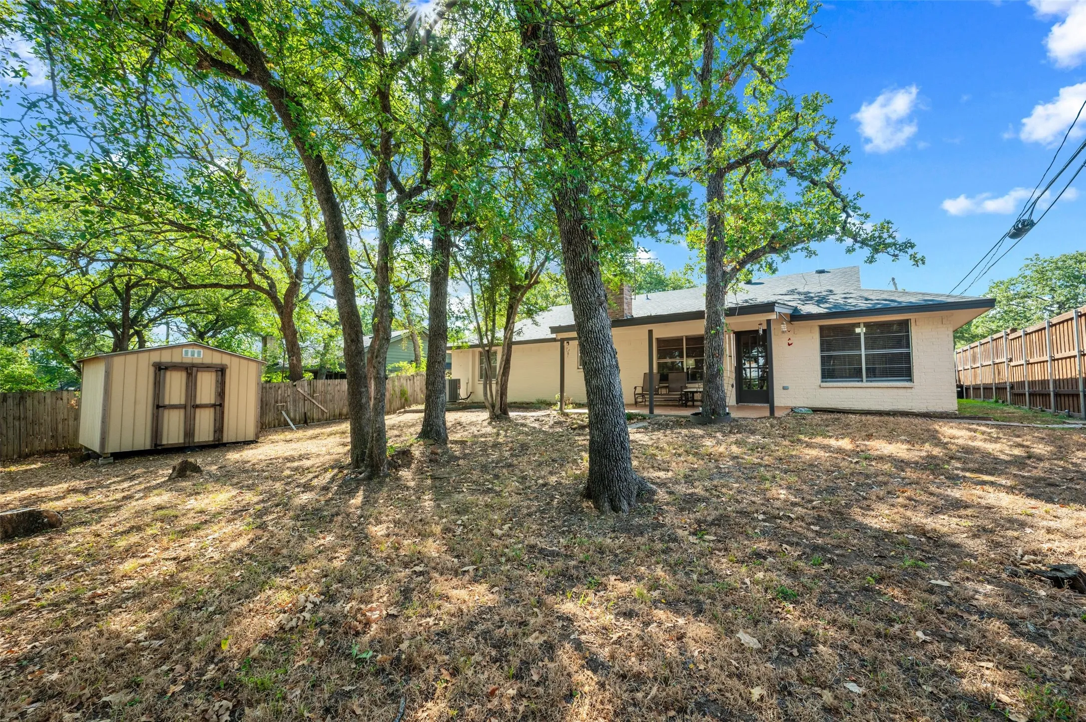 Expansive backyard with a storage shed, mature trees, wood privacy fencing, and an exterior patio