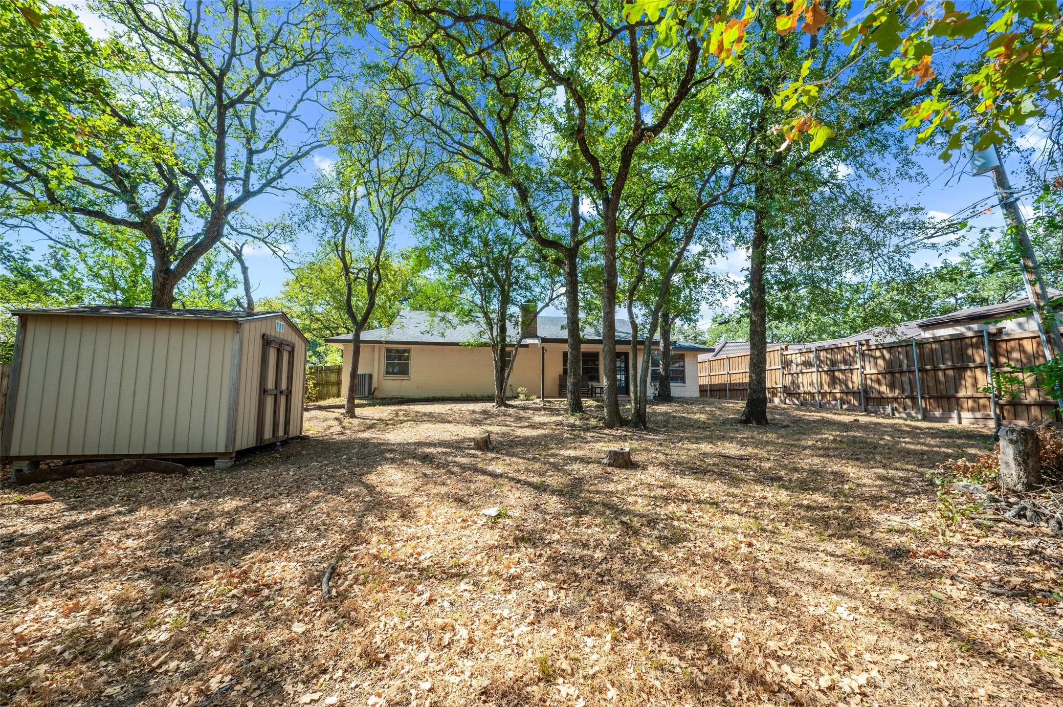 Expansive rear yard featuring mature trees, a detached storage shed, and perimeter fencing
