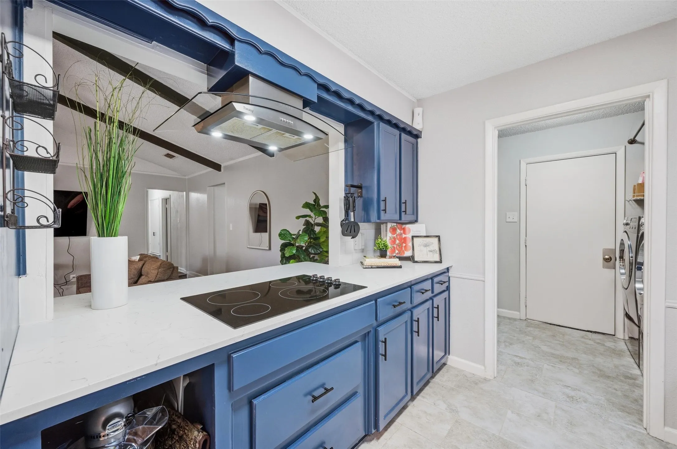 White countertop with integrated cooktop, blue cabinetry, range hood, and tile flooring