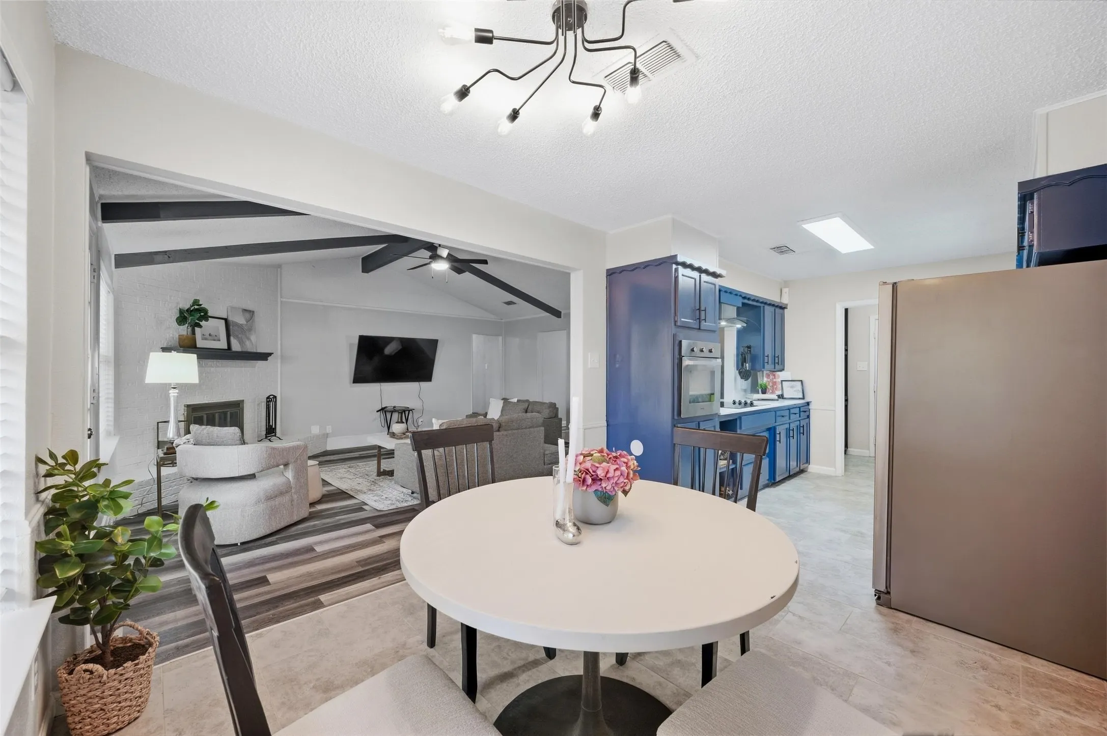 Open-concept layout featuring a kitchen with blue cabinetry and stainless steel appliances, a dining area, and a living space with vaulted ceilings and a fireplace