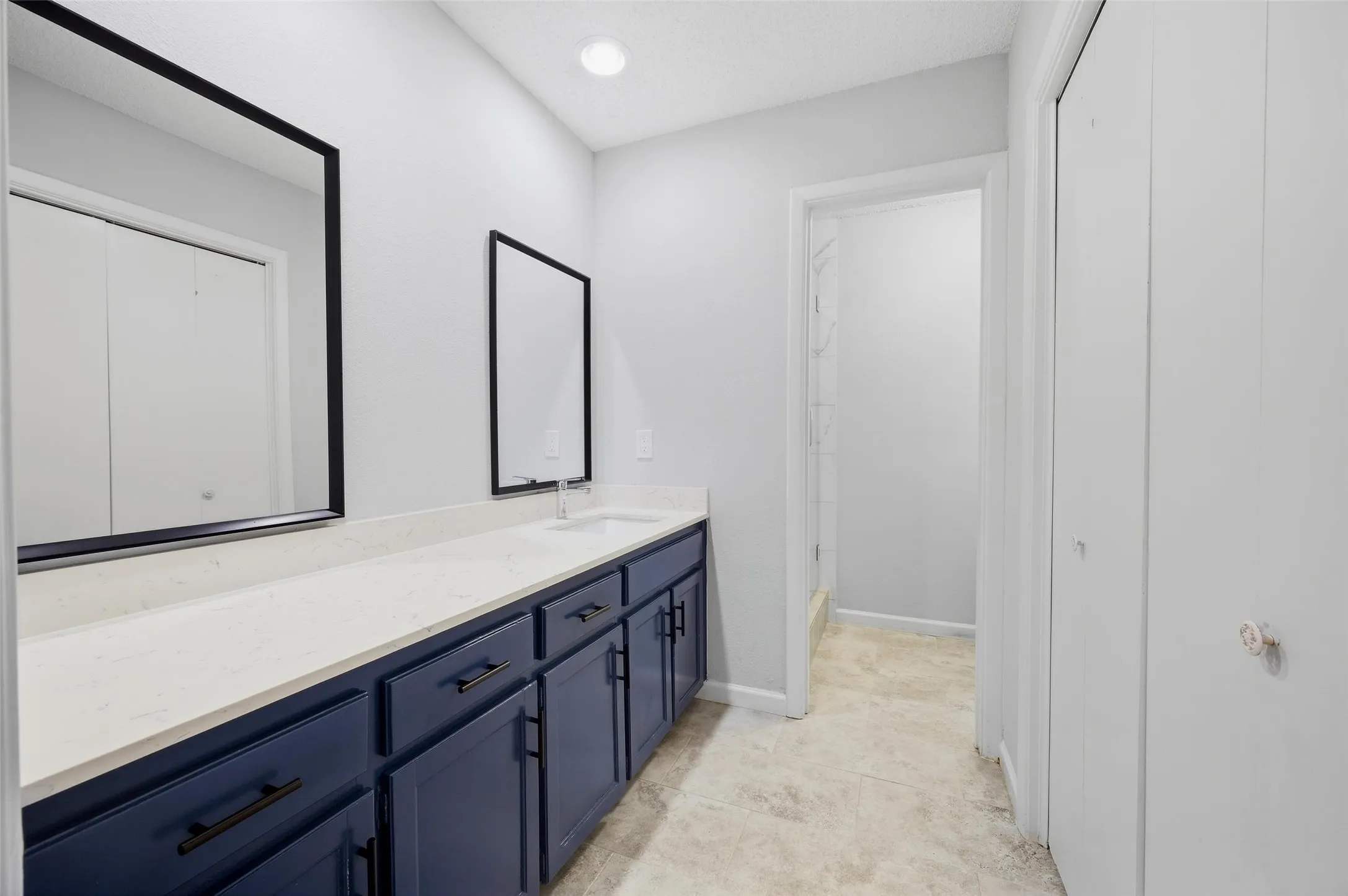 Dual basin vanity with blue cabinetry, light-toned countertop, and modern black framed mirrors