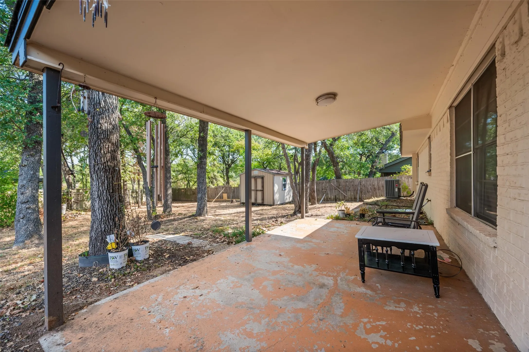 Covered concrete patio with overhead lighting, featuring a brick exterior wall and a detached shed in the background