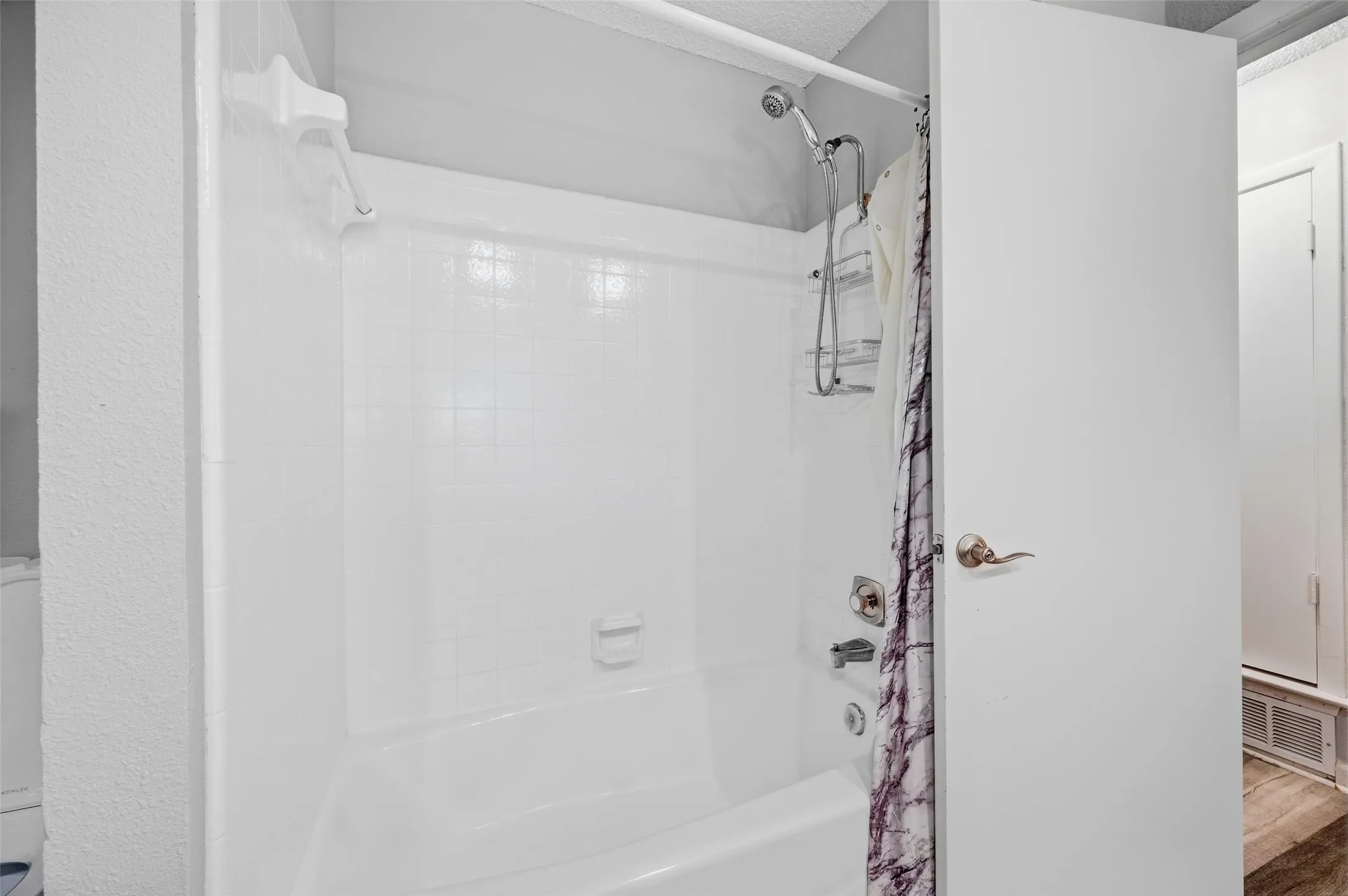 Bathtub with integrated shower, white tiled surround, and chrome fixtures