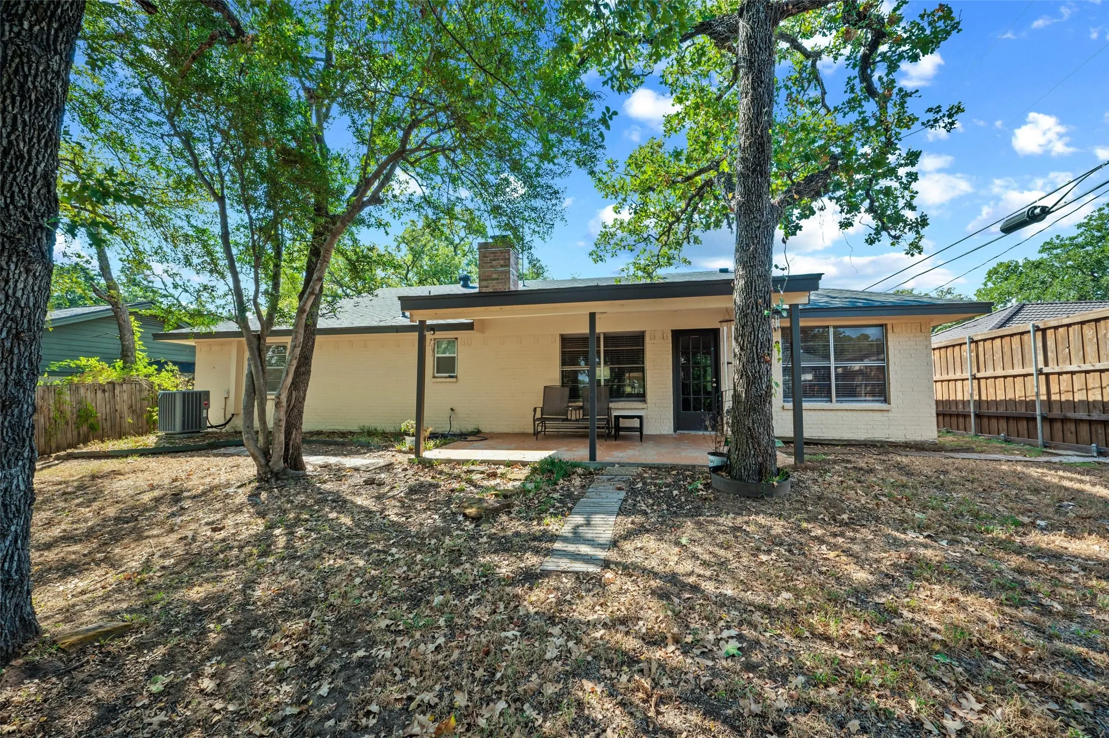 Exterior featuring a covered patio, brick chimney, privacy fencing, and mature trees