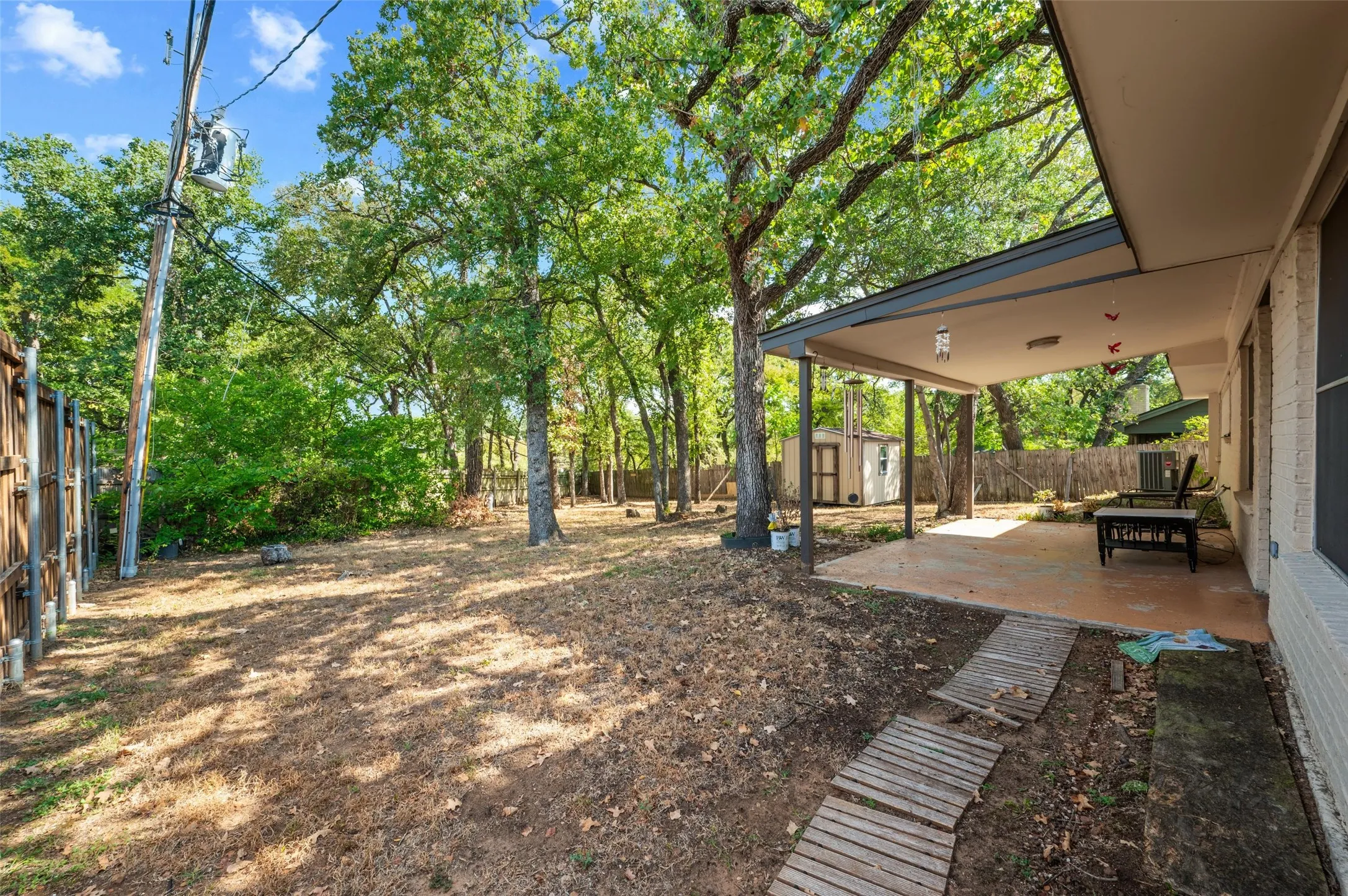Expansive backyard with a covered patio, privacy fencing, mature trees, and a storage shed