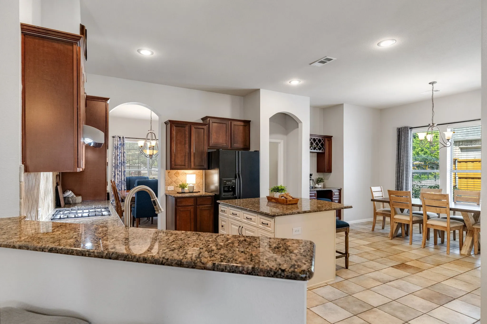 The open kitchen features granite countertops, solid maple cabinetry, recessed lighting, an oversized kitchen island with seating, and tile flooring extending into the breakfast area.