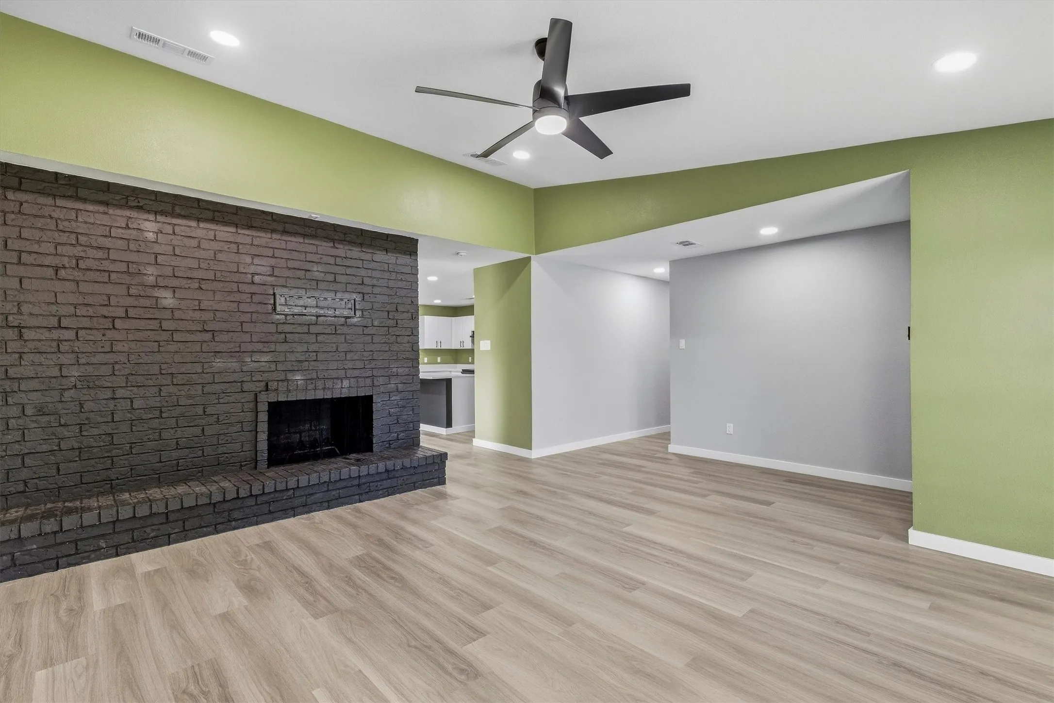 Expansive room featuring a painted brick fireplace, wood-finish flooring, recessed lighting, and a ceiling fan