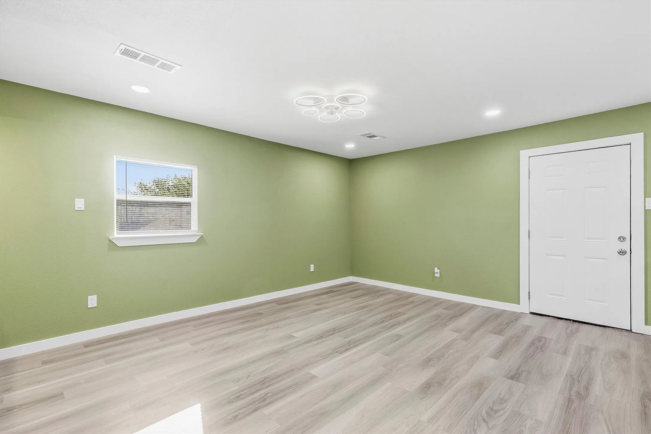 Wood-finish flooring, recessed lighting, modern ceiling fixture, single window, and a paneled door