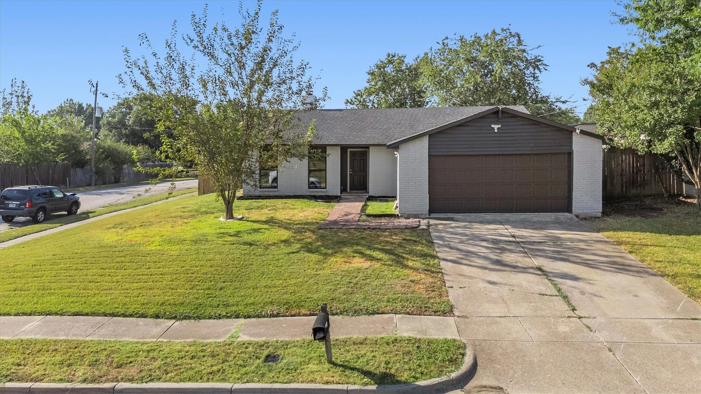 Single-story residence featuring a two-car garage, concrete driveway, and a front lawn with a mature tree