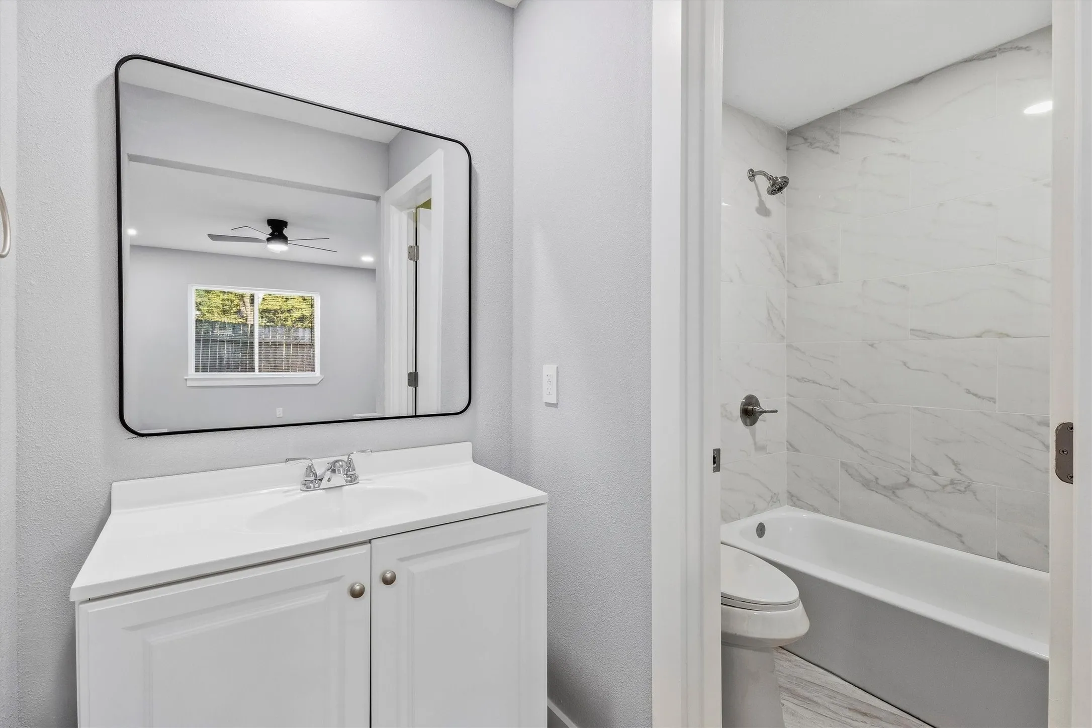 White vanity with integrated sink, rectangular mirror with rounded corners, white wall tiling, and chrome fixtures