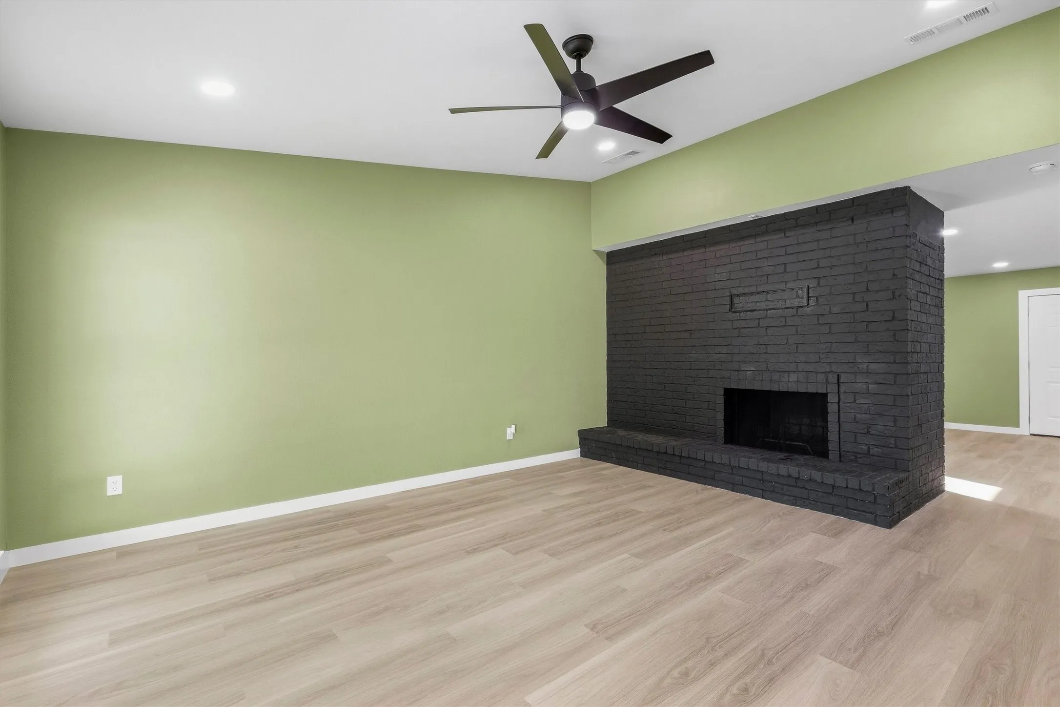 Light wood-finish flooring, recessed lighting, and a black brick fireplace feature with a hearth