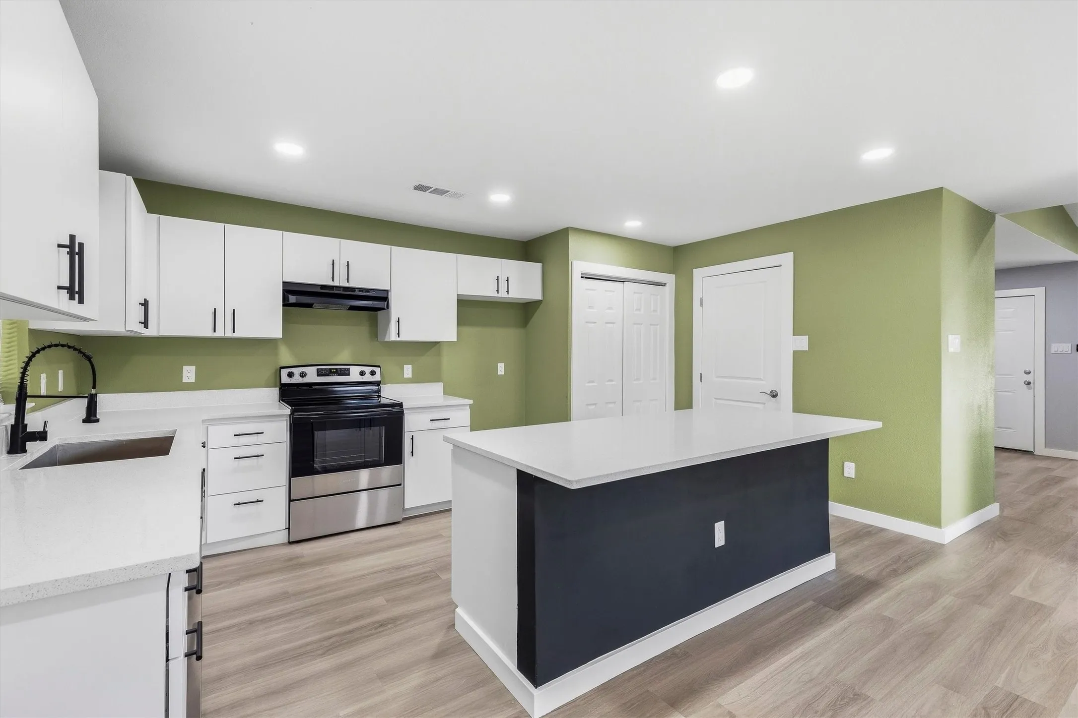 Kitchen featuring white cabinetry, stainless steel range, light-toned wood-finish flooring, a central island with a white countertop, and recessed lighting