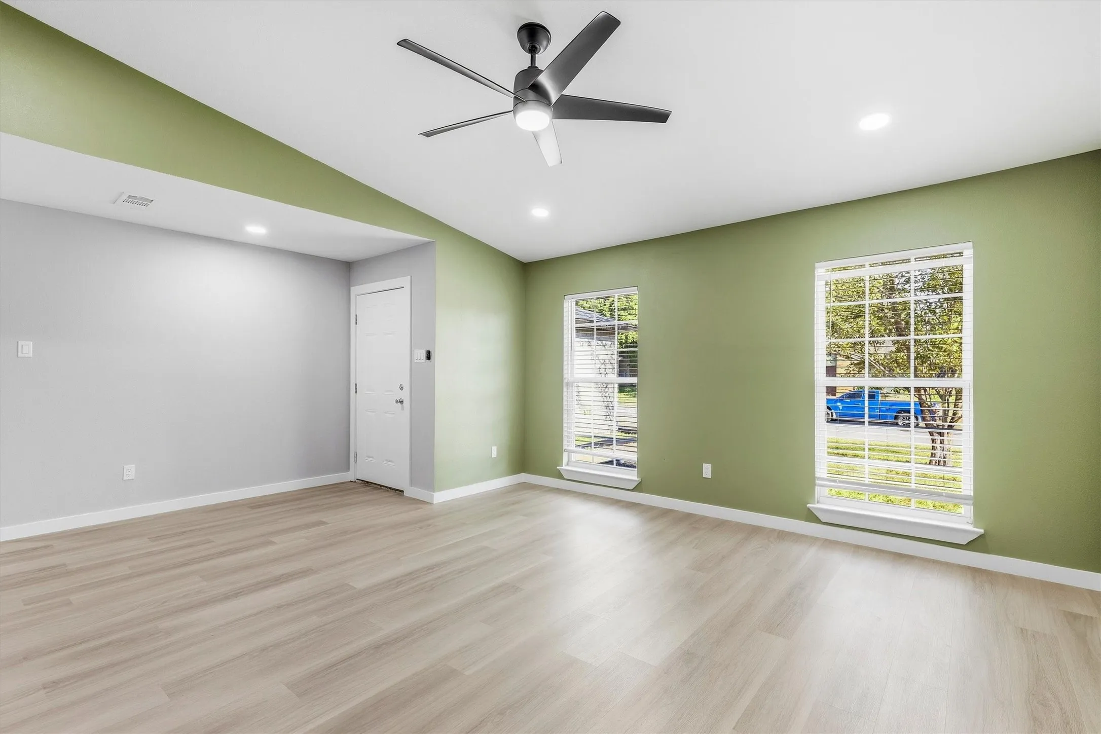 Vaulted ceiling with a ceiling fan and recessed lighting, light wood-finish flooring, and multiple windows