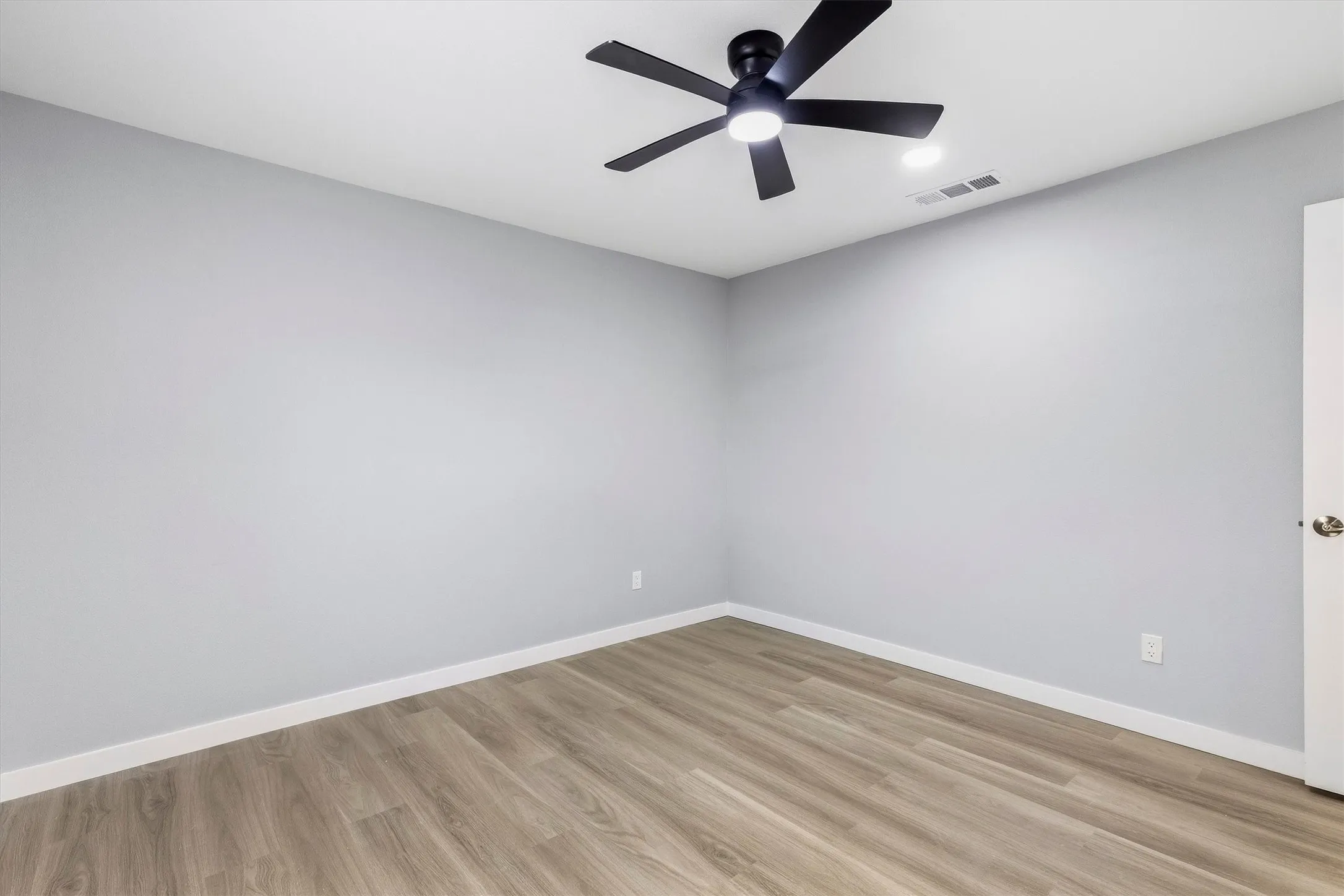 Wood-finish flooring, white walls, and a contemporary black ceiling fan with integrated lighting