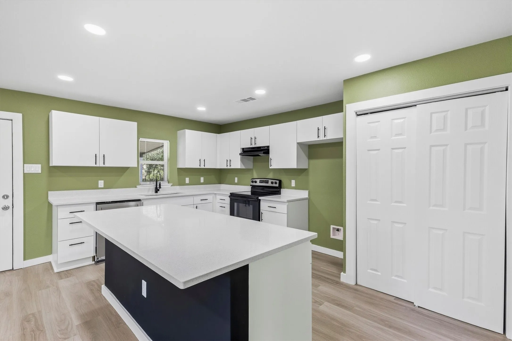 Modern kitchen featuring white cabinetry, a central island with a solid surface countertop, recessed lighting, and wood-finish flooring