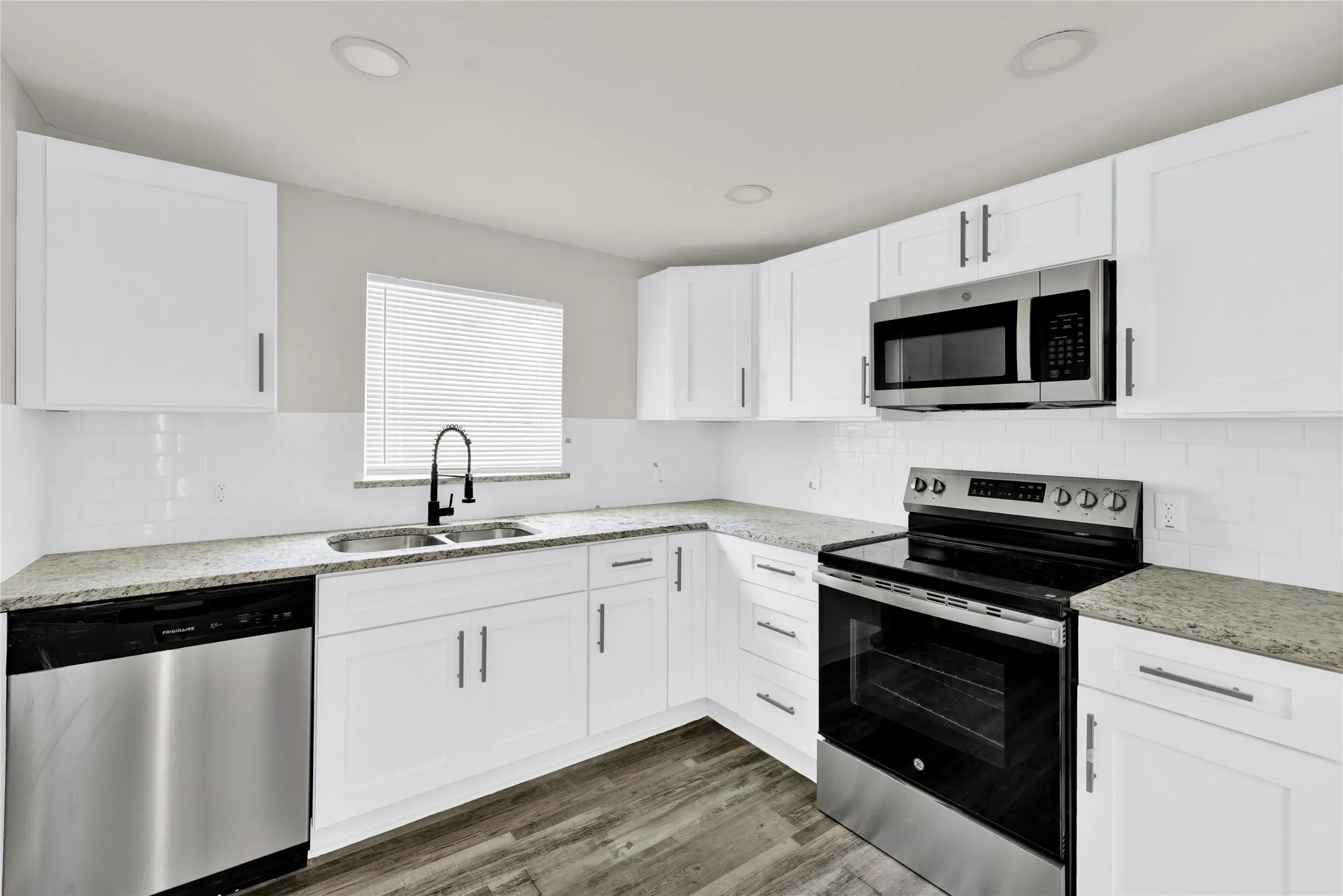 Kitchen featuring white cabinetry, light-toned countertops, stainless steel appliances, a white subway tile backsplash, and wood-finish flooring
