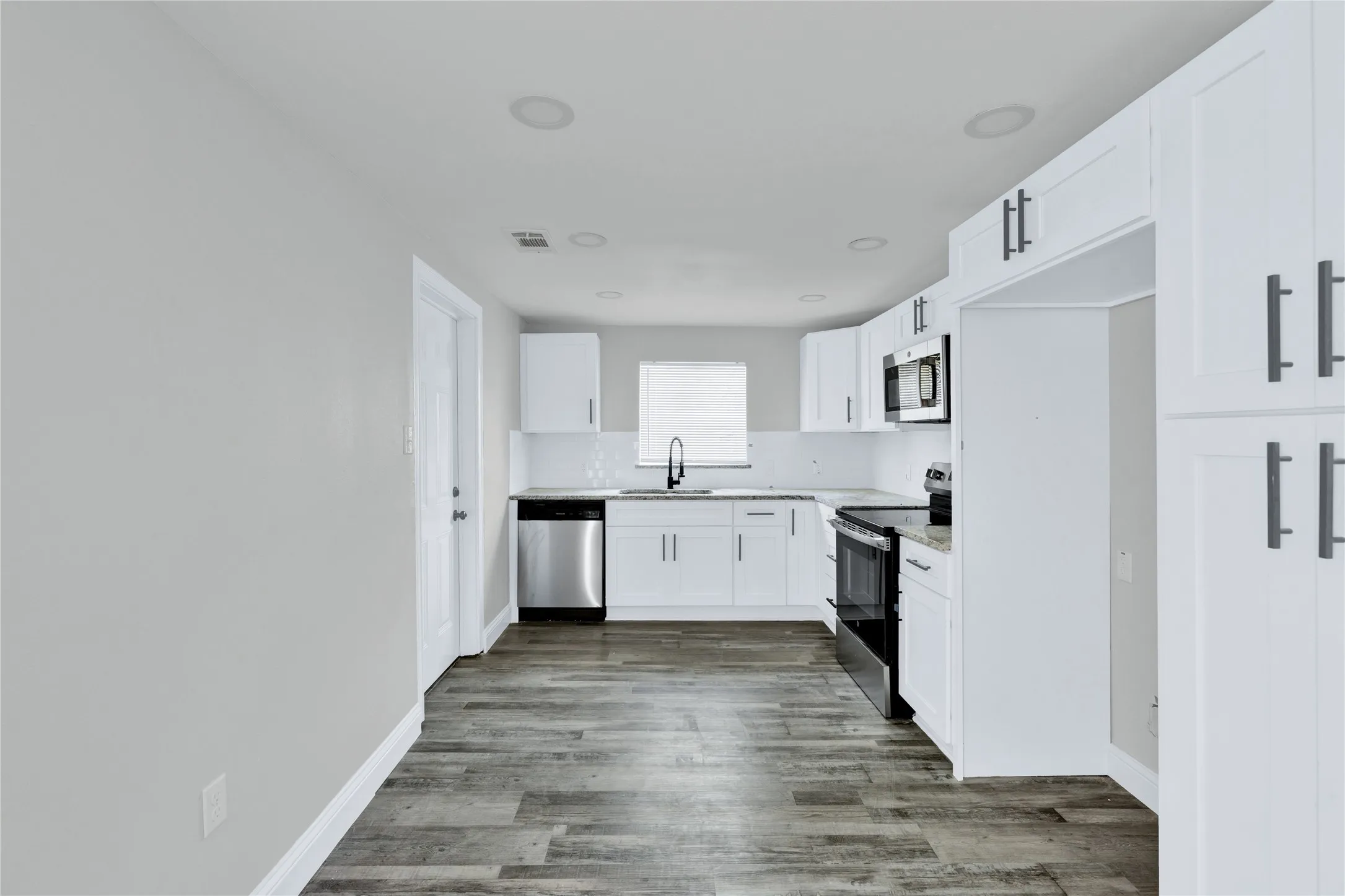 Modern kitchen featuring white cabinetry, wood-finish flooring, stainless steel appliances, and recessed lighting