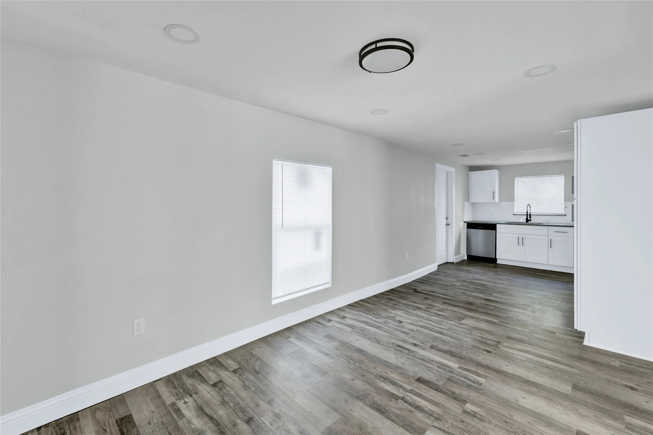 Wood-finish flooring throughout, recessed ceiling lighting, a modern flush-mount ceiling fixture, white kitchen cabinetry, and stainless steel kitchen appliances