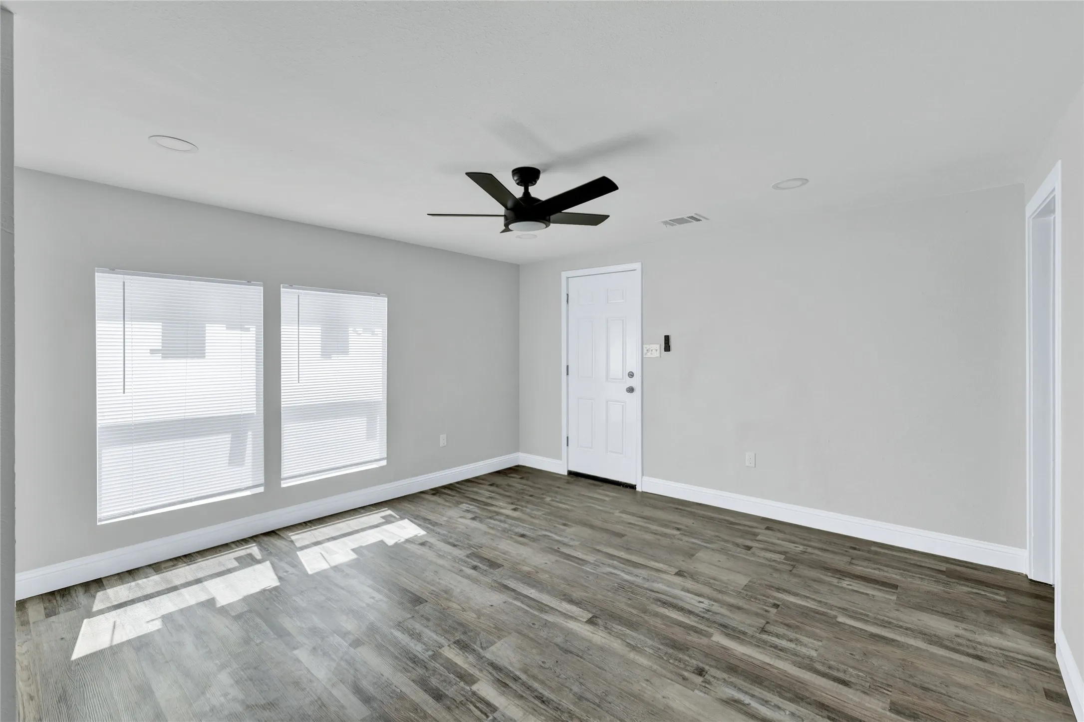 Spacious room featuring wood-finish flooring, two large windows with blinds, a ceiling fan, and recessed lighting