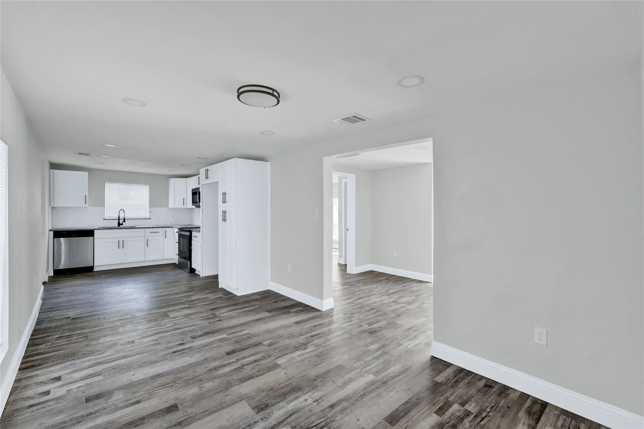 Open-concept kitchen and living area featuring wood-finish flooring, white cabinetry, black countertops, and recessed lighting