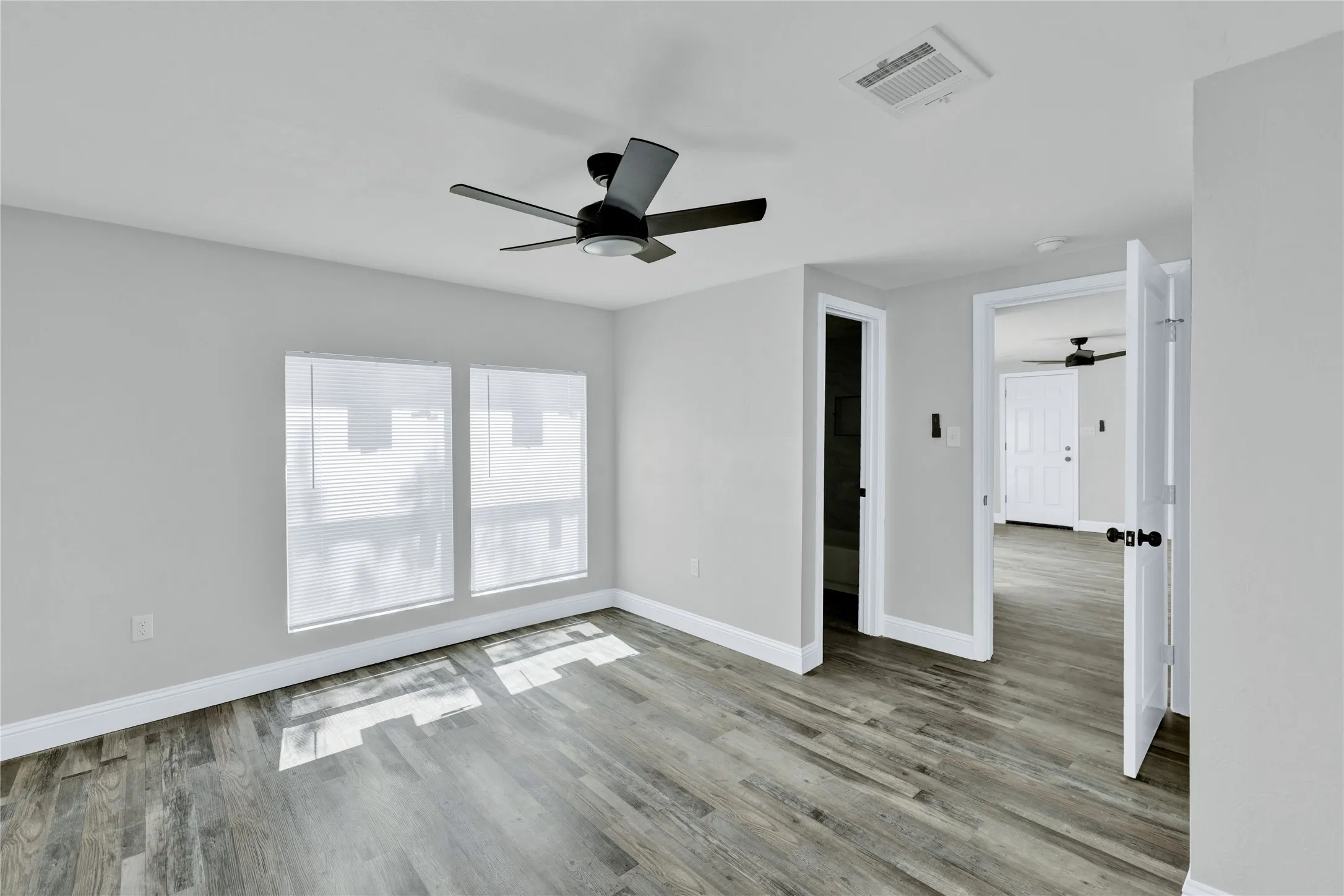 Wood-finish flooring, two large windows, white walls, black ceiling fan, and white trim