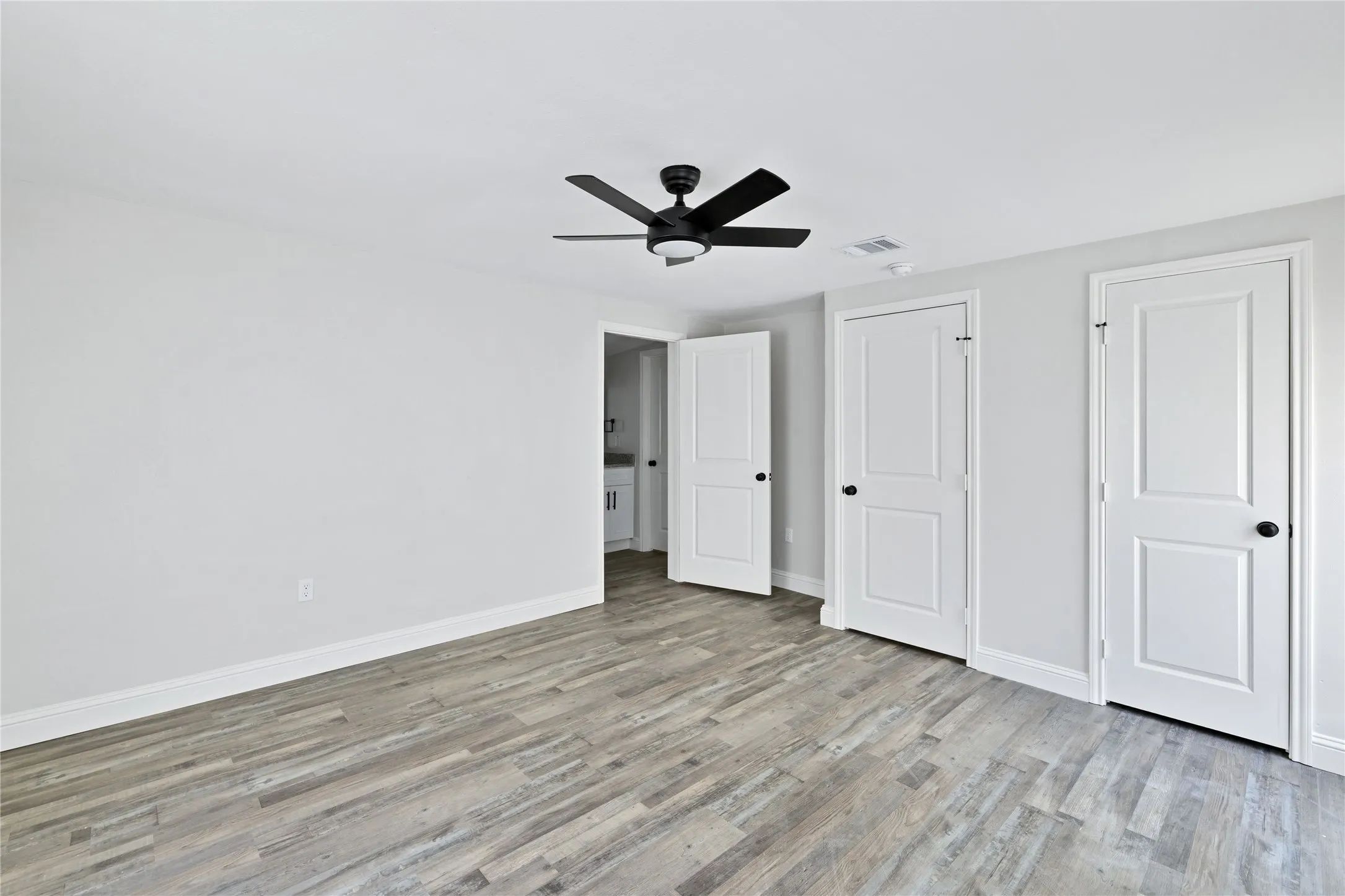 Wood-finish flooring with a flush baseboard, white interior walls, and a matte black ceiling fan