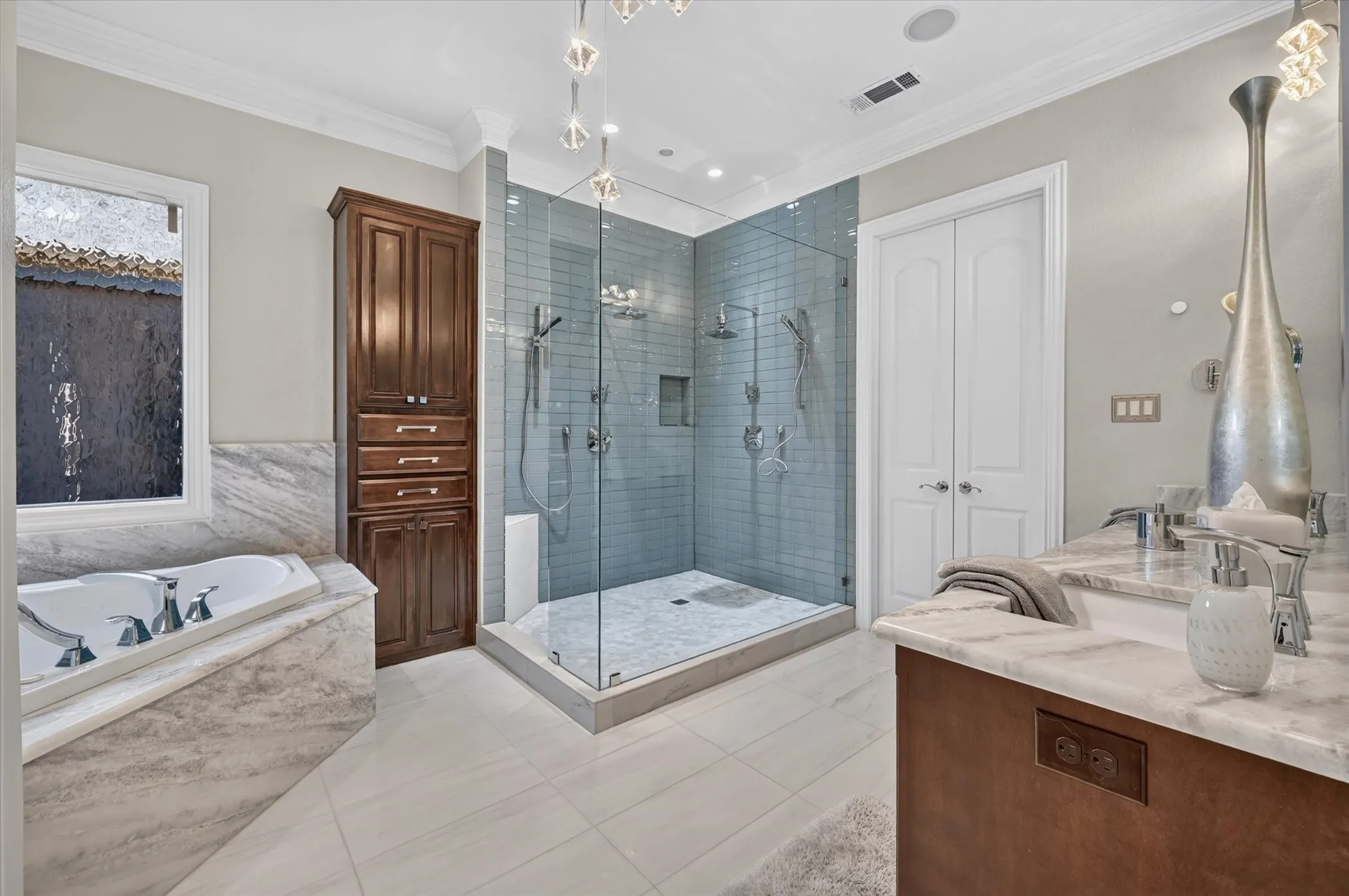 Walk-in shower with glass enclosure and light blue tile, built-in bathtub with stone surround, wood-finish cabinetry, dual vanity with stone countertop, and crown molding