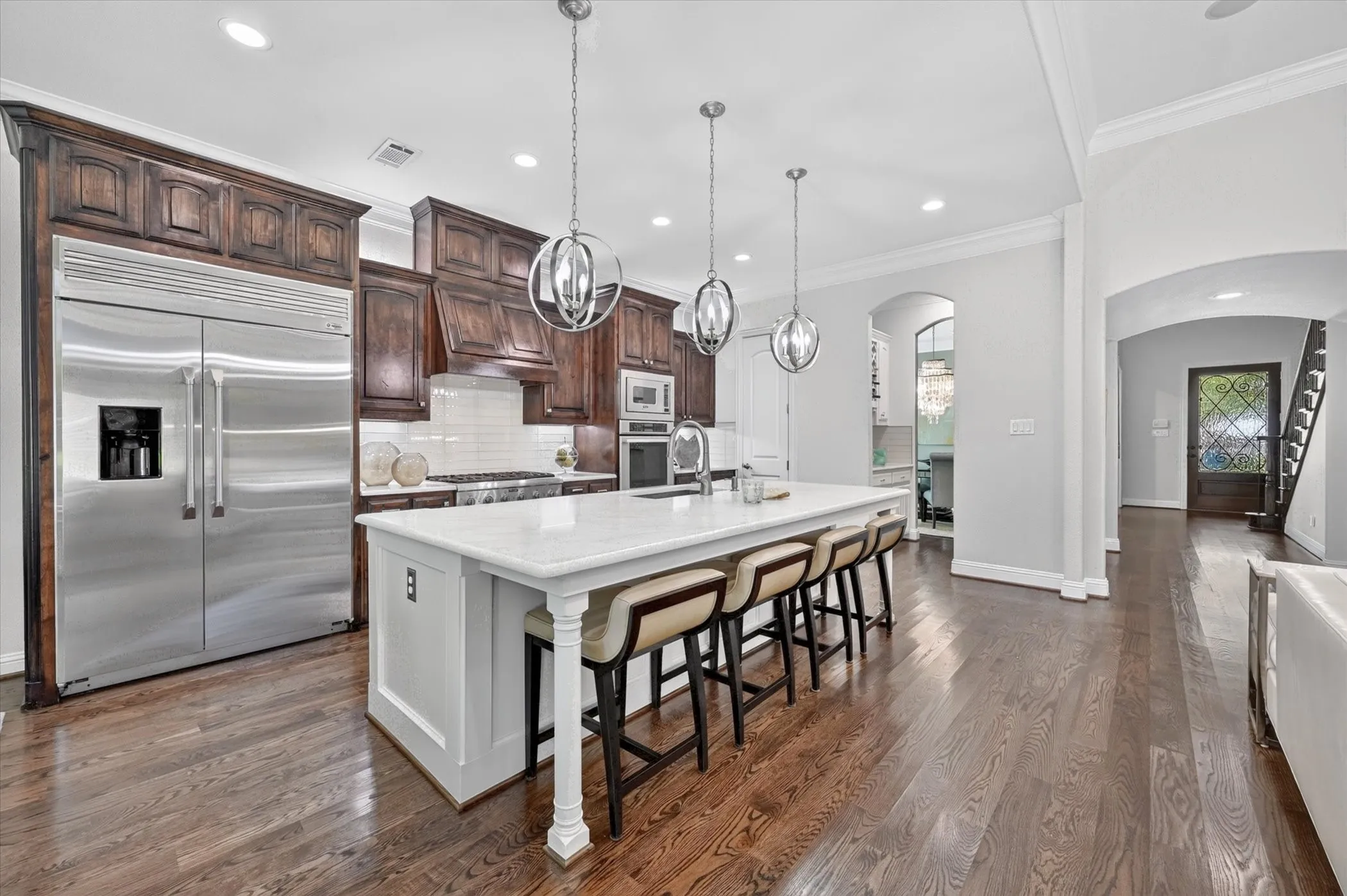 Gourmet kitchen featuring a large central island with seating, stainless steel appliances, dark wood cabinetry, and wood-finish flooring