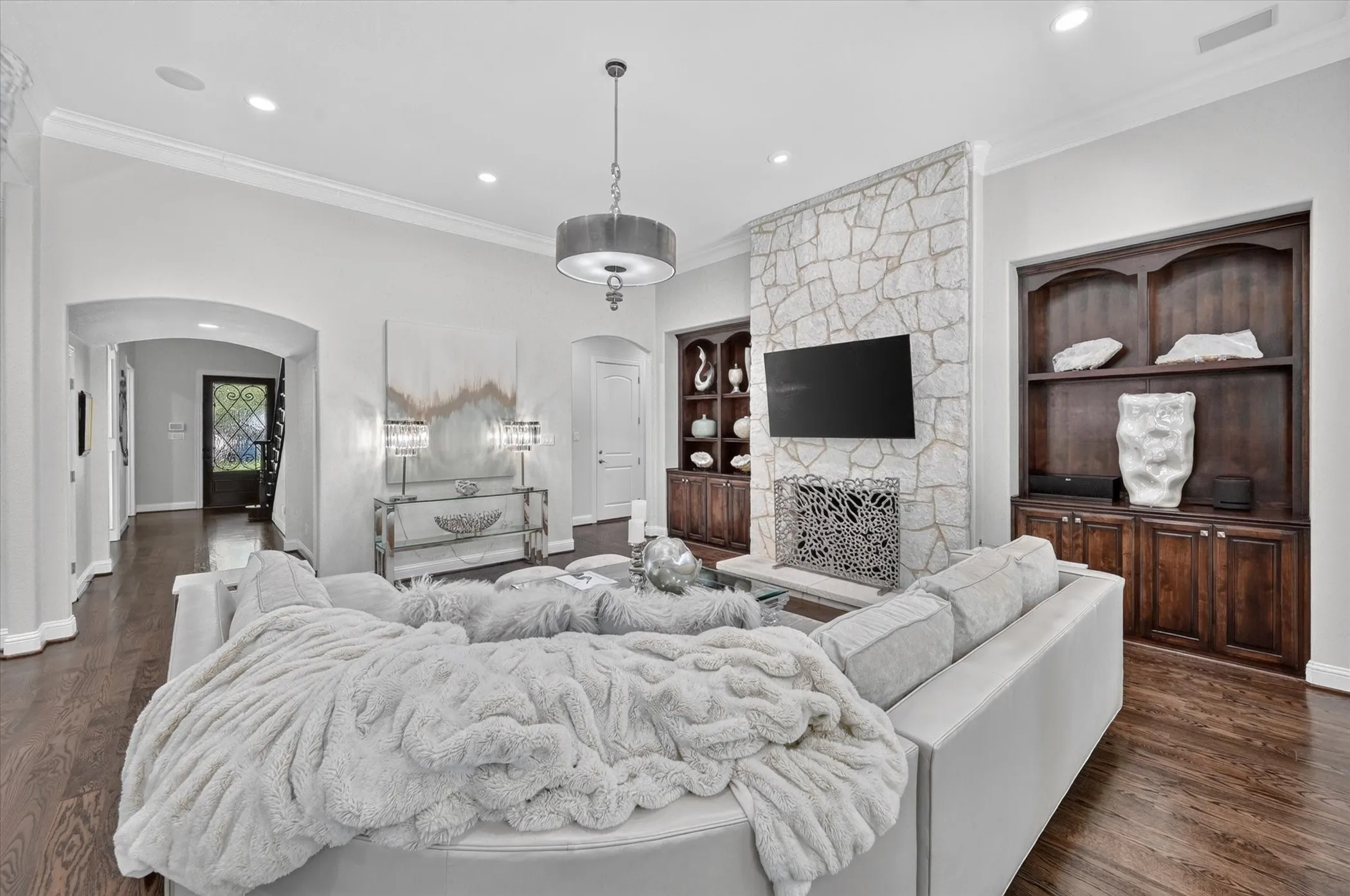 Stone-faced fireplace, dark wood-finish flooring, built-in shelving, recessed lighting, and a drum pendant light fixture