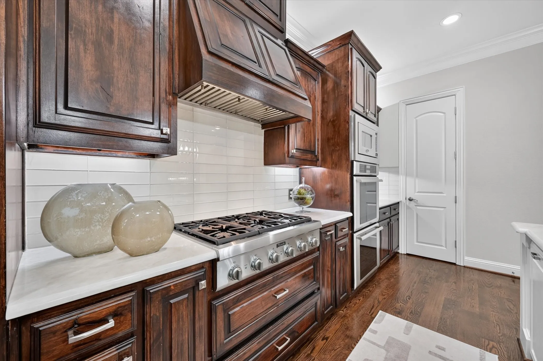 Custom dark wood cabinetry, white subway tile backsplash, professional-grade range, built-in double ovens, and recessed lighting