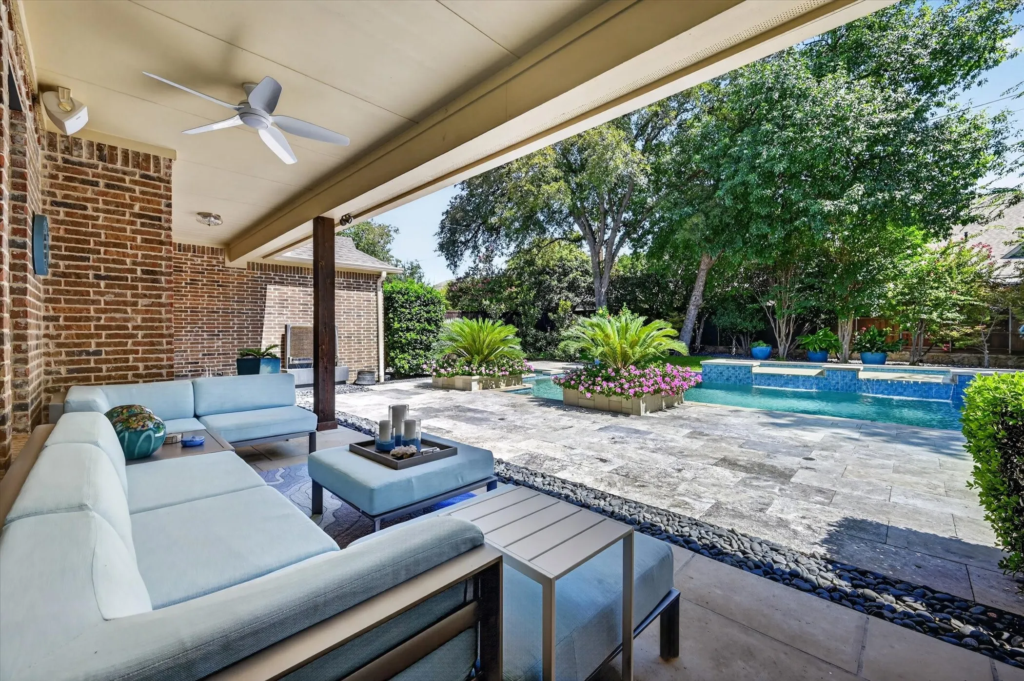 Covered patio with brick exterior, ceiling fan, and stone-tiled flooring