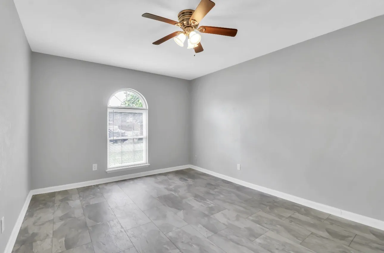 Spacious room featuring light gray walls, wood-finish flooring, and a ceiling fan with integrated lighting