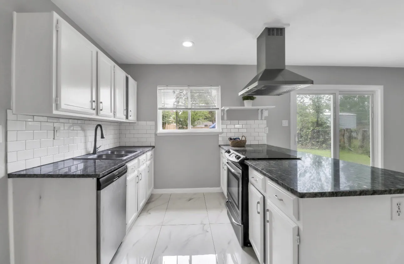 Modern kitchen featuring white cabinetry, dark stone countertops, subway tile backsplash, stainless steel appliances, and a sliding glass door
