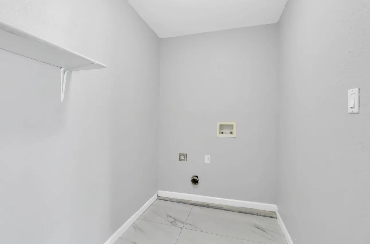 Dedicated utility space featuring light gray walls, a built-in white shelf, and light-toned tile flooring