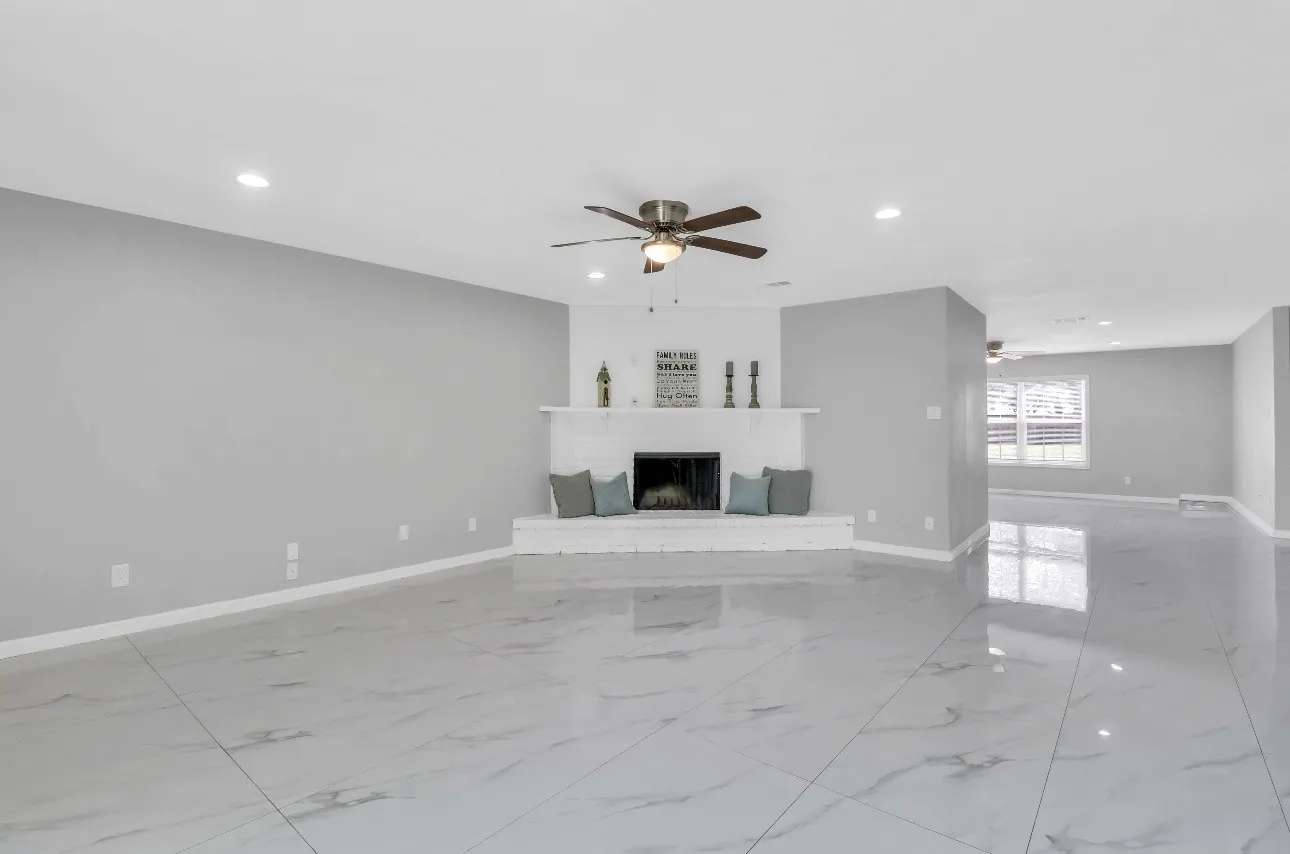 Spacious living area featuring a white brick fireplace with mantel, ceiling fan, recessed lighting, and large format tile flooring