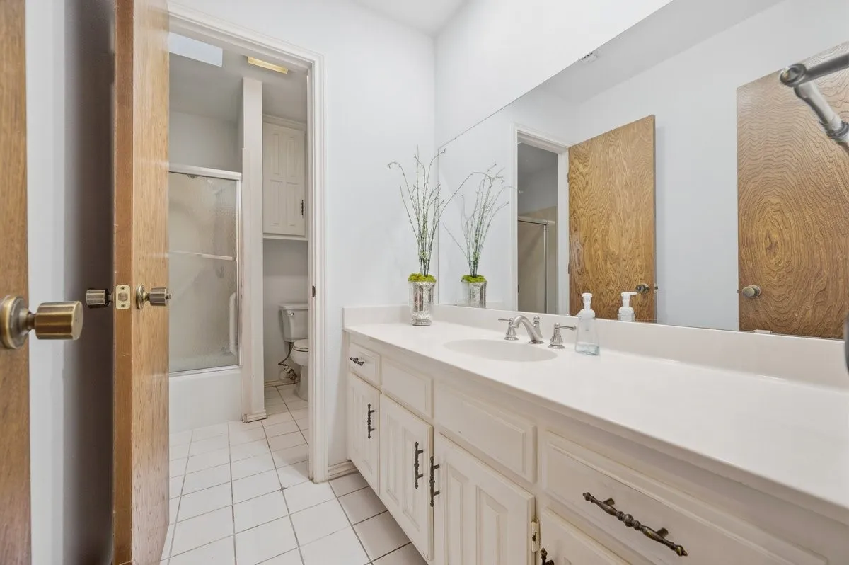 Double vanity with integrated sink, expansive wall mirror, and white cabinetry with dark hardware