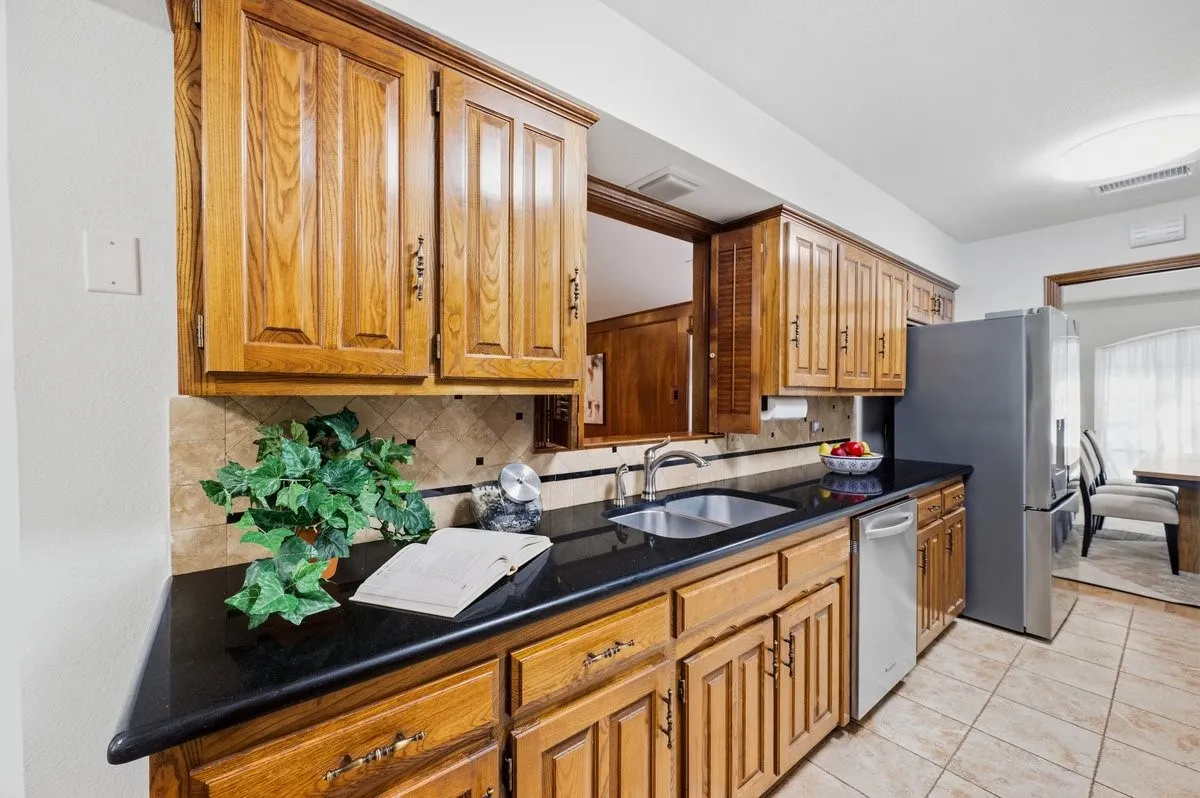 Wood cabinetry with dark countertops, tile backsplash, and stainless-steel appliances