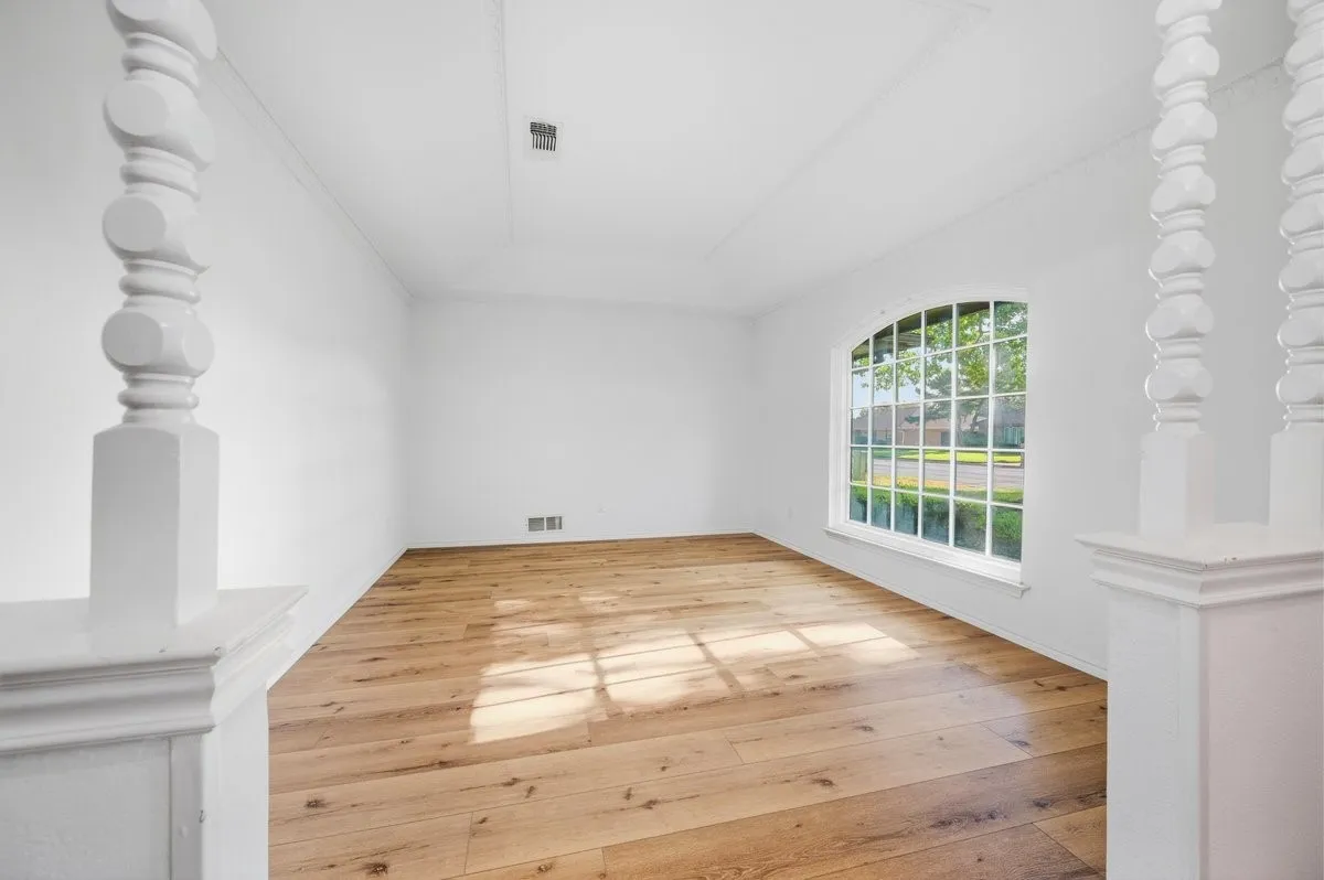Wood-finish flooring, white walls, arched window with grilles, and decorative white balusters