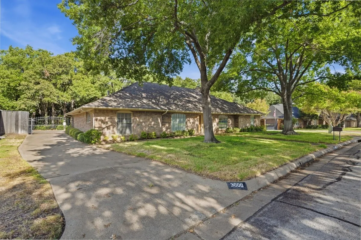Brick exterior, mature trees, manicured lawn, paved driveway, and wrought iron gate