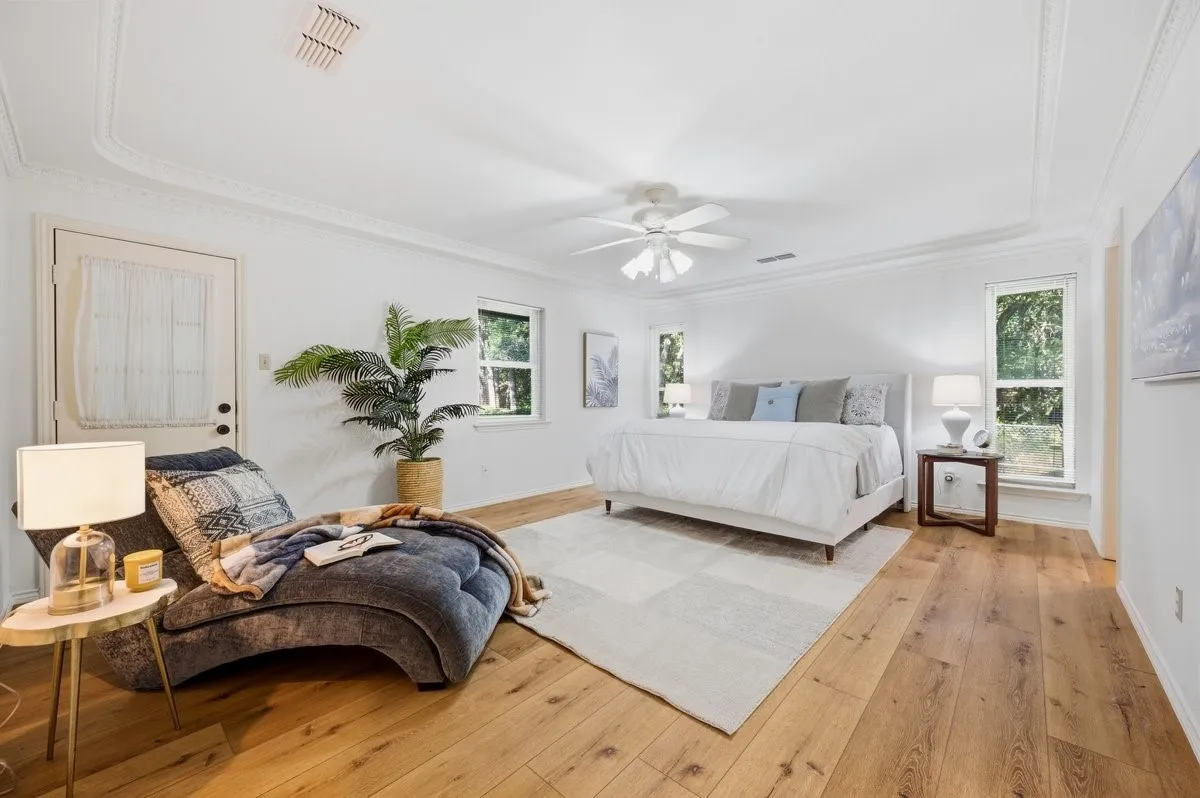 Wood-finish flooring, white walls, tray ceiling, crown molding, and a ceiling fan