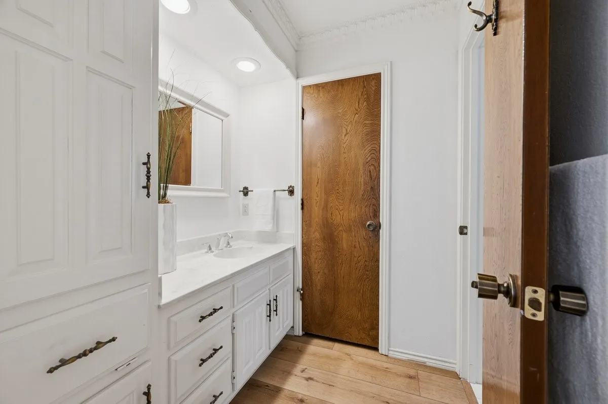 White vanity with integrated sink and chrome fixtures, framed mirror, recessed lighting, wood-finish flooring, and crown molding