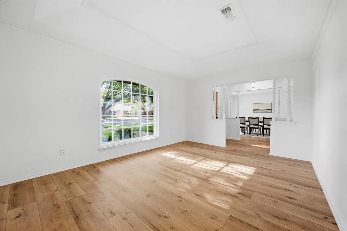 Arched window with grilles, tray ceiling, crown molding, wood-finish flooring, and a pass-through opening to an adjacent room